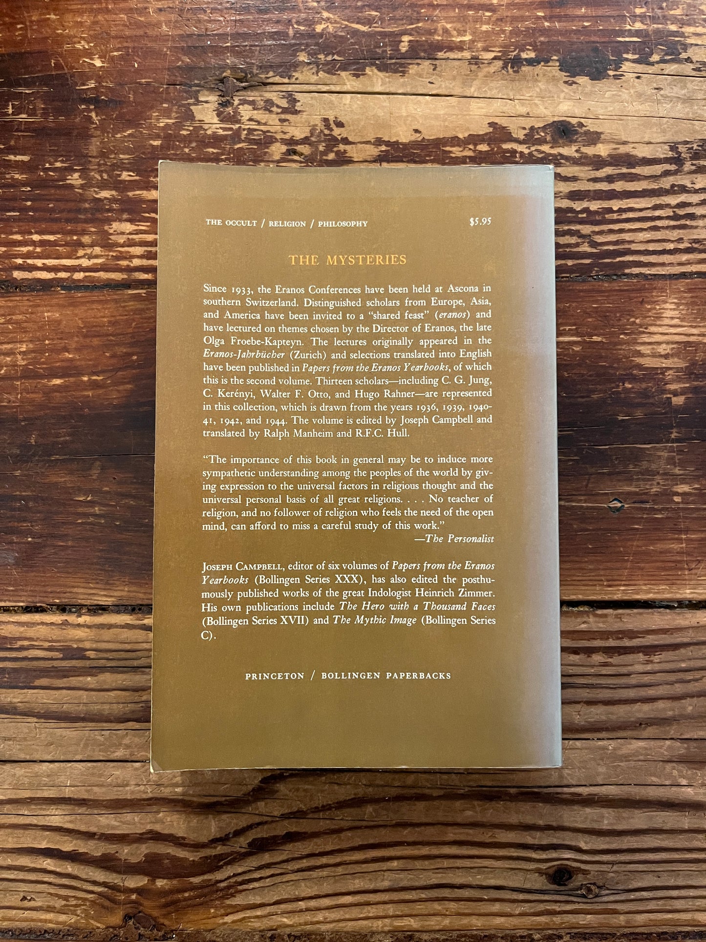 Back cover of book titled 'The Mysteries, papers from the Eranos Yearbooks' on a wooden surface