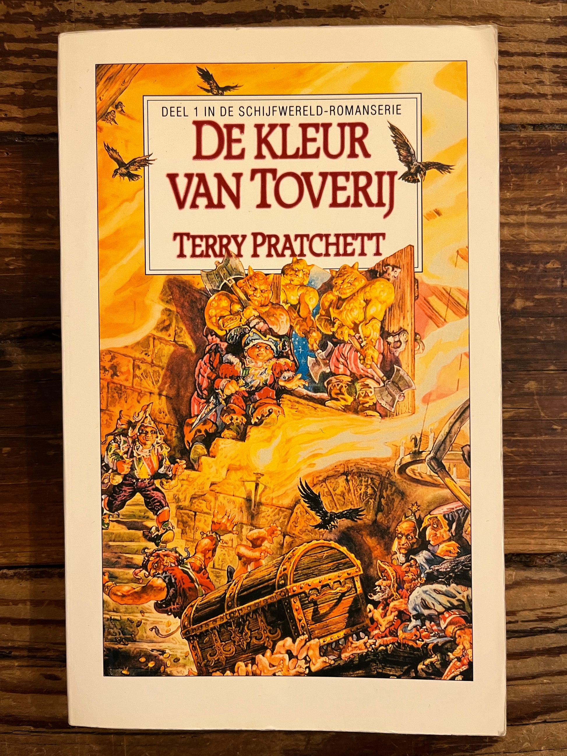 Voorkant van boek met de titel 'de kleur van Toverij' door Terry Prachett op houten achtergrond