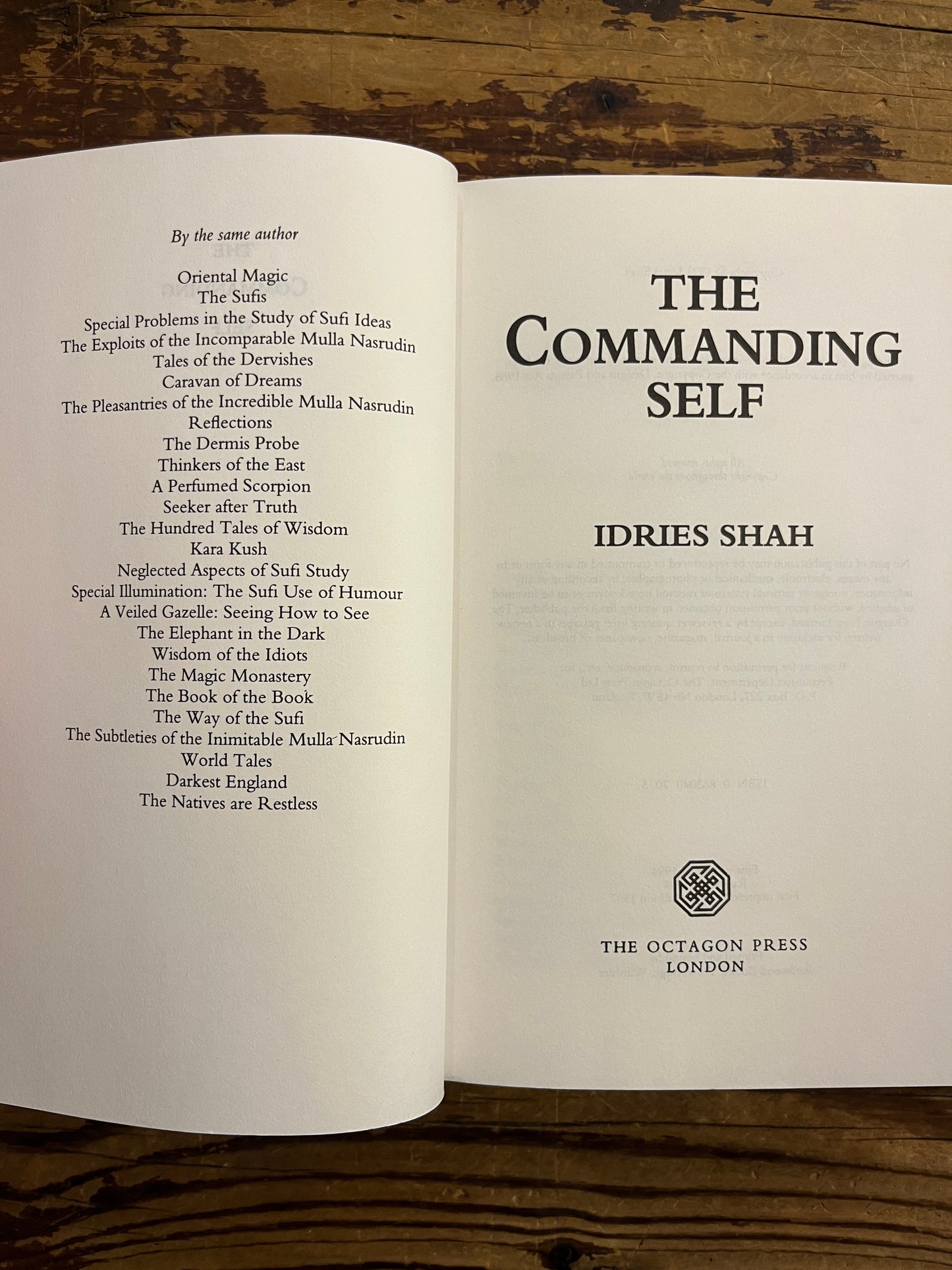 Open book titled 'The Commanding Self' by Idries Shah on a wooden surface