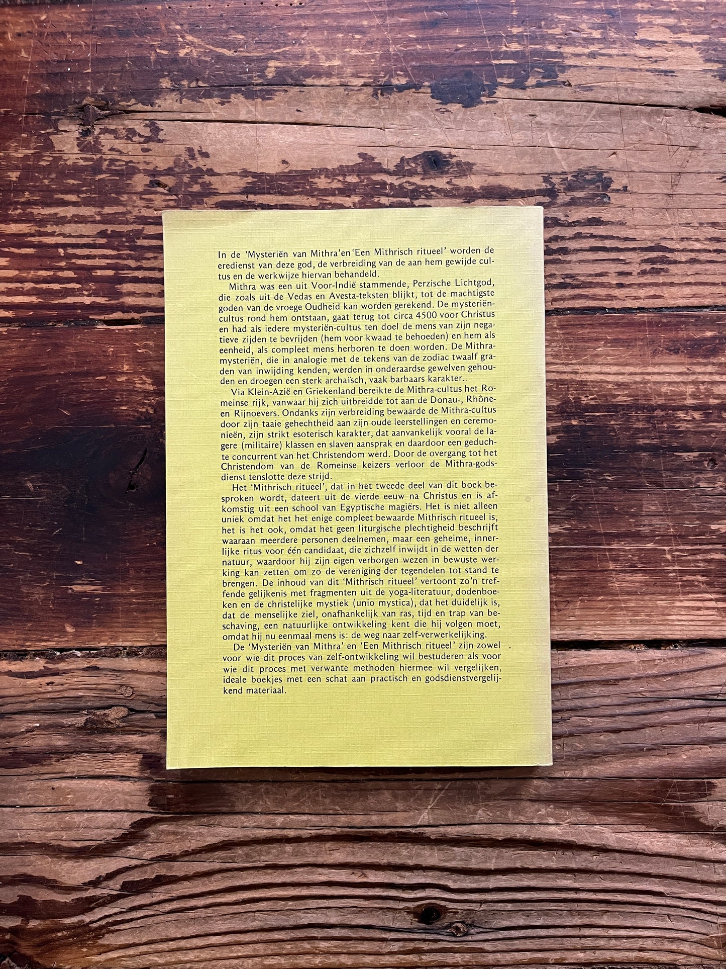 Achterkant van boek met de titel 'De Mysteriën van Mithra en een Mithrisch Ritueel' op een houten achtergrond