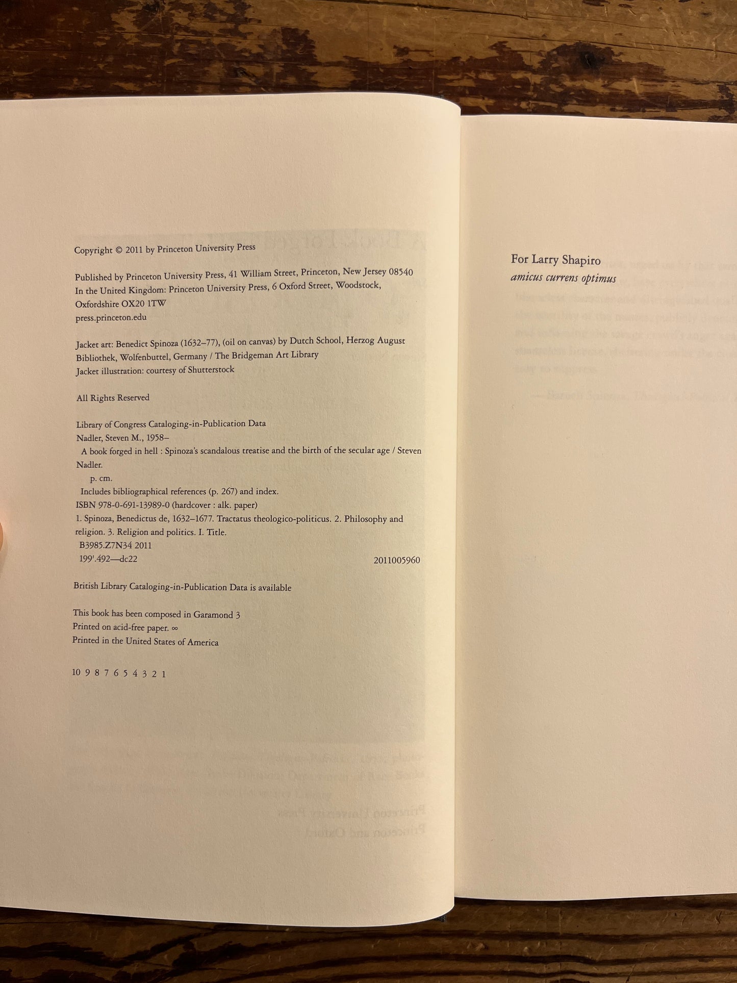 open book titled 'A Book Forged in Hell' by Steven Nadler on a wooden surface