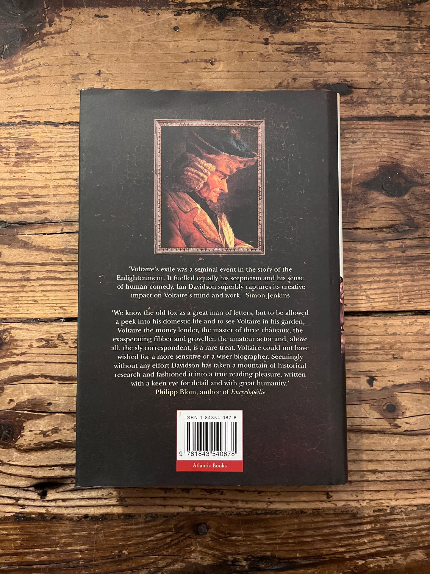Photo of the backcover of the book "Voltaire in exile" on a wooden background
