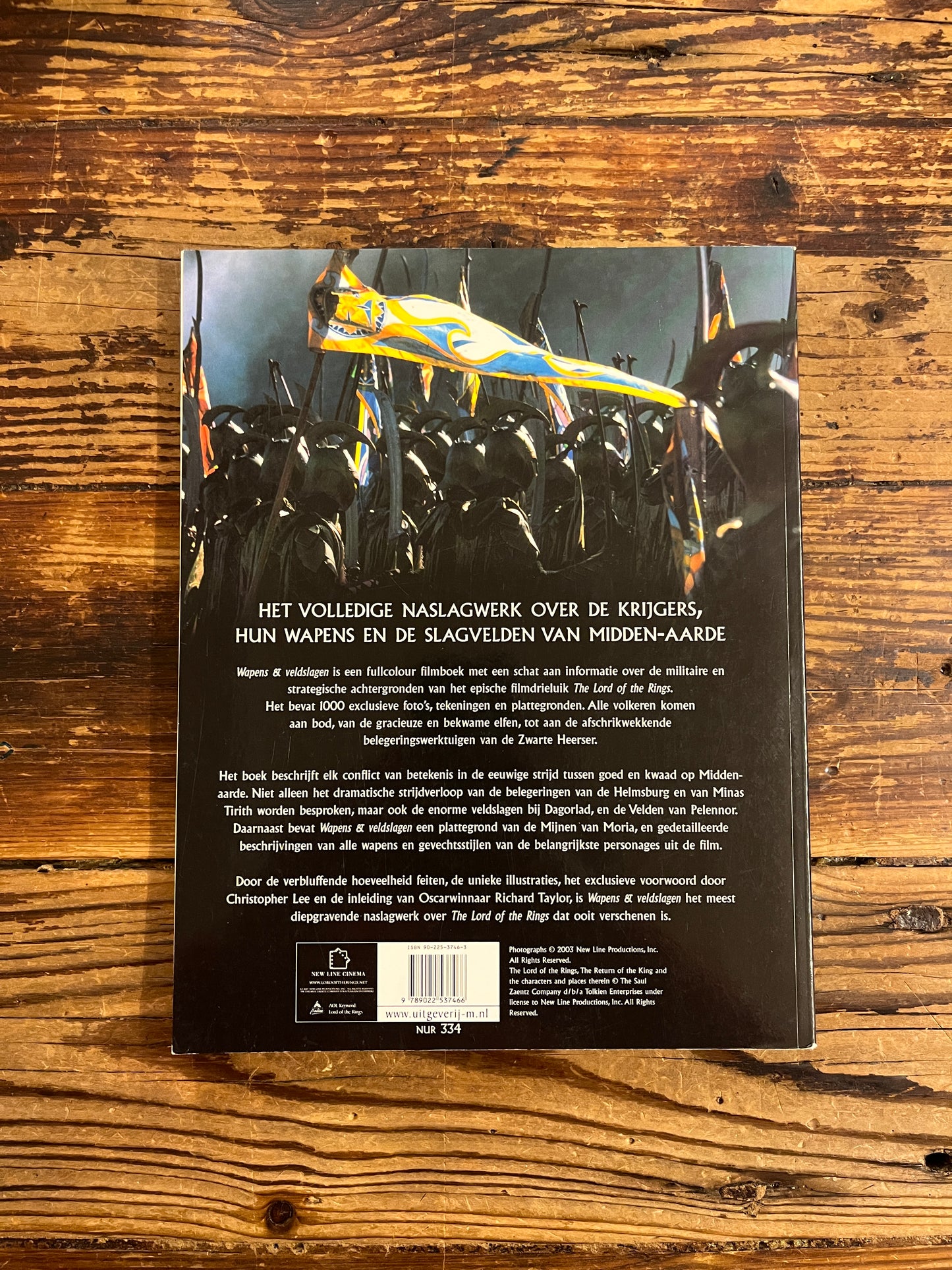 Achterkant van boek met de titel 'the lord of the rings, wapens en veldslagen' op een houten achtergrond