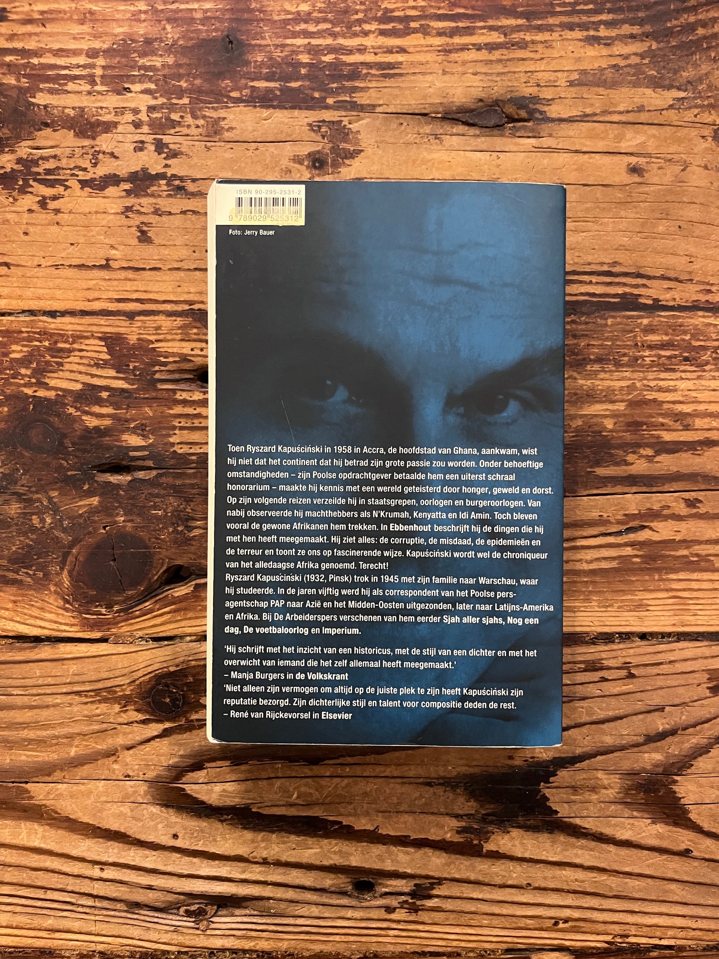 Achterkant van boek met de titel 'ddenhout' door Ryszard Kapuscinski op een houten achtergrond