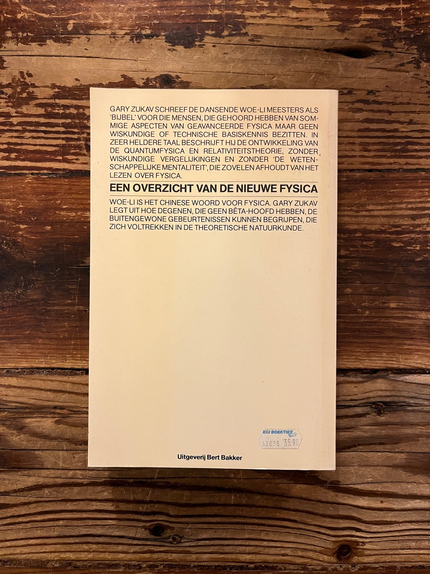 Achterkant van boek met de titel 'De Dansende Woe-Li Meesters' door Gary Zukav op een houten achtergrond