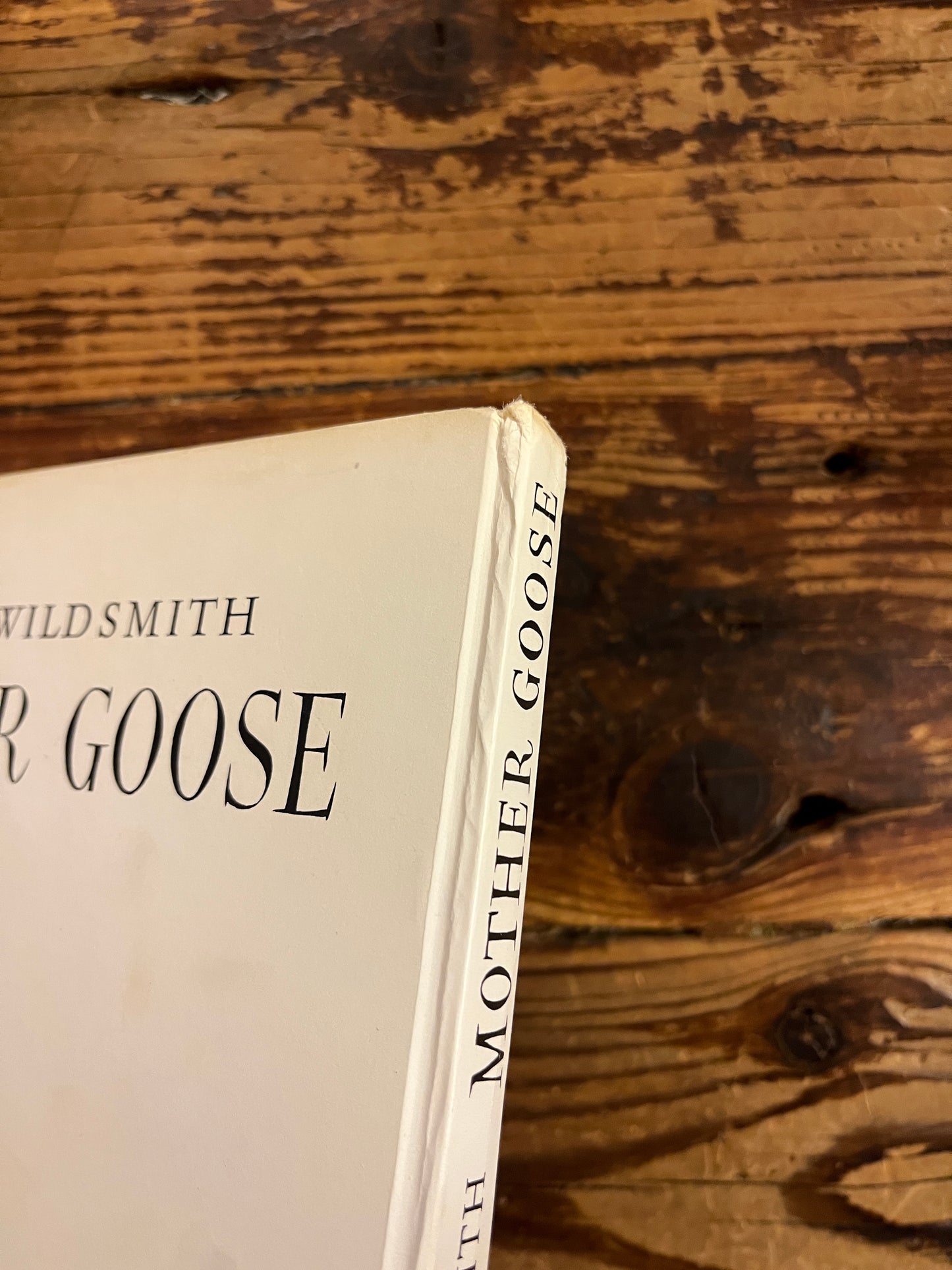 Top op book titled 'Mother Goose' by Brian Wild Smith showing a light bumb on the spine on a wooden surface