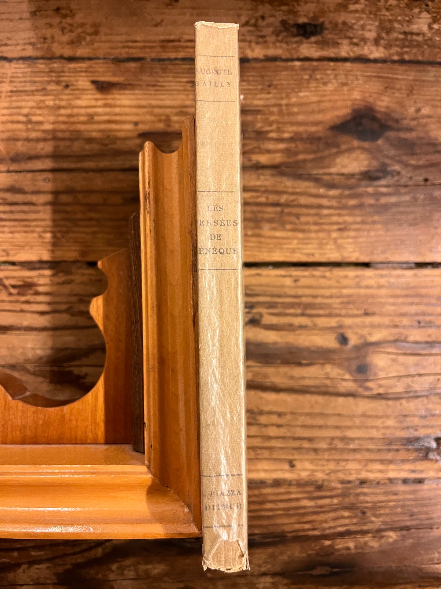 dos du livre "Les pensées de sénèque" sur fond de bois et soutenu par un calle livre en bois