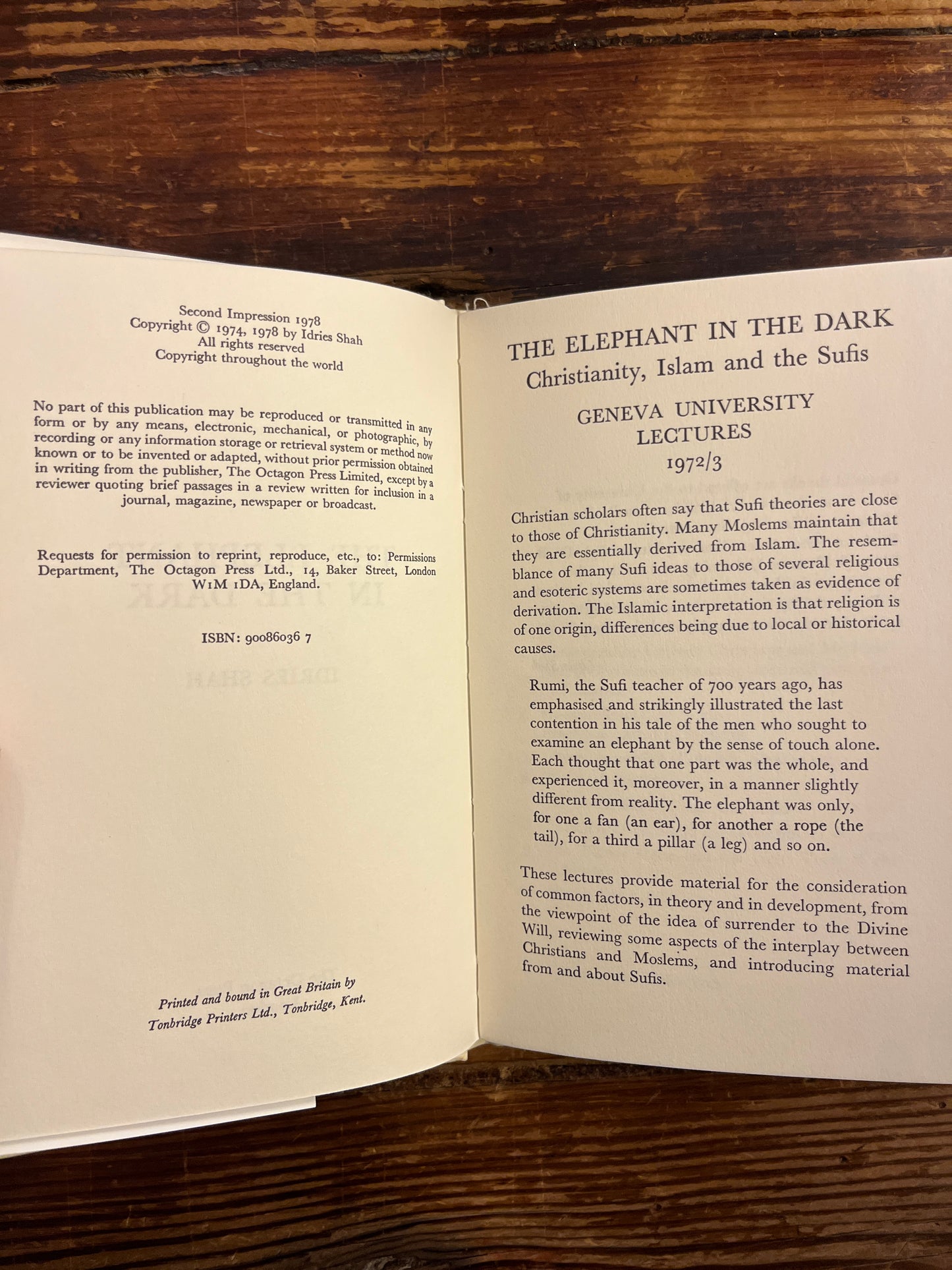 Open book titled 'the elephant in the dark' by Idries Shah with text on a wooden surface