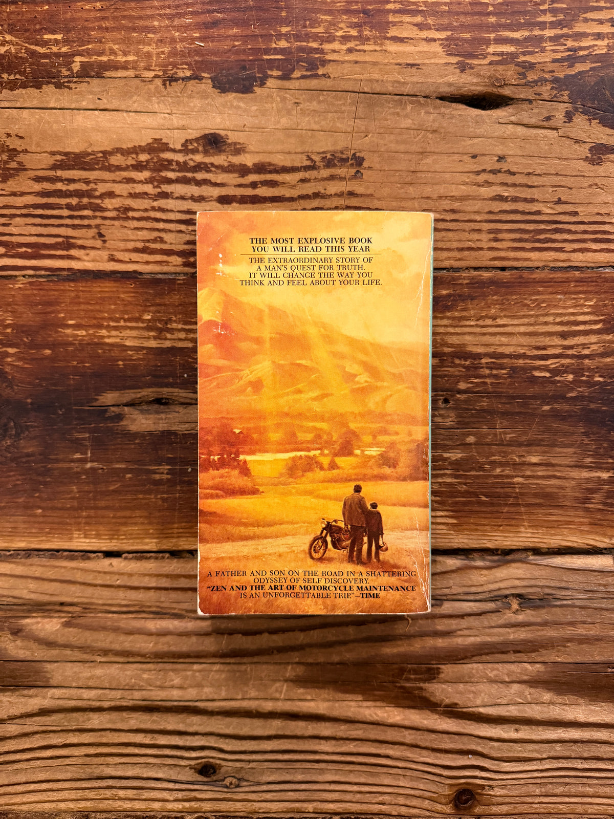 Back cover of a book titled 'Zen and the Art of Motorcycle Maintenance' by Robert M. Pirsig on a wooden surface
