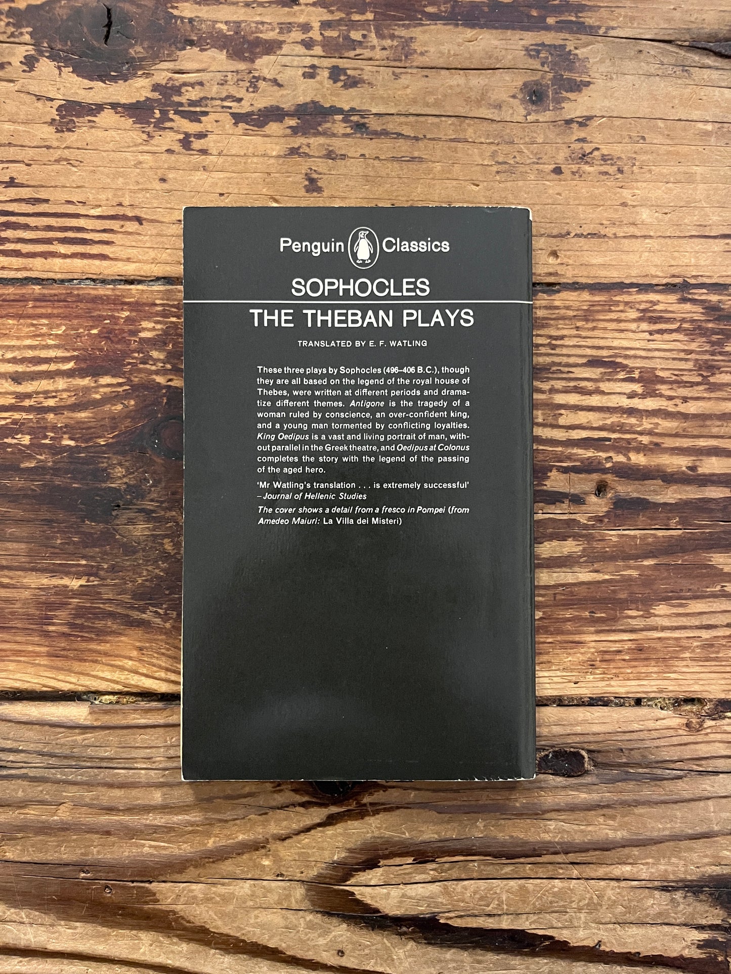 Back cover of 'the theban plays' by Sophocles on a wooden surface