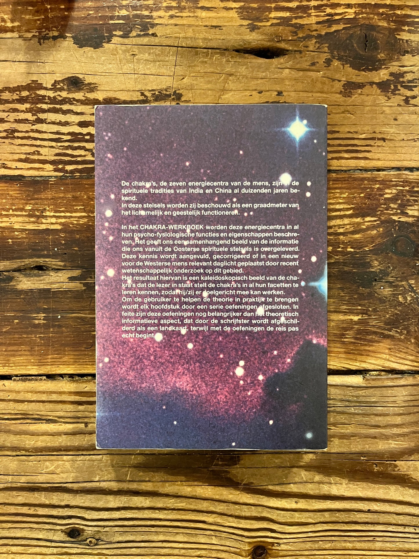 Achterkant van boek met de titel 'Chakra werkboek' door Andrea Judith op een houten achtergrond