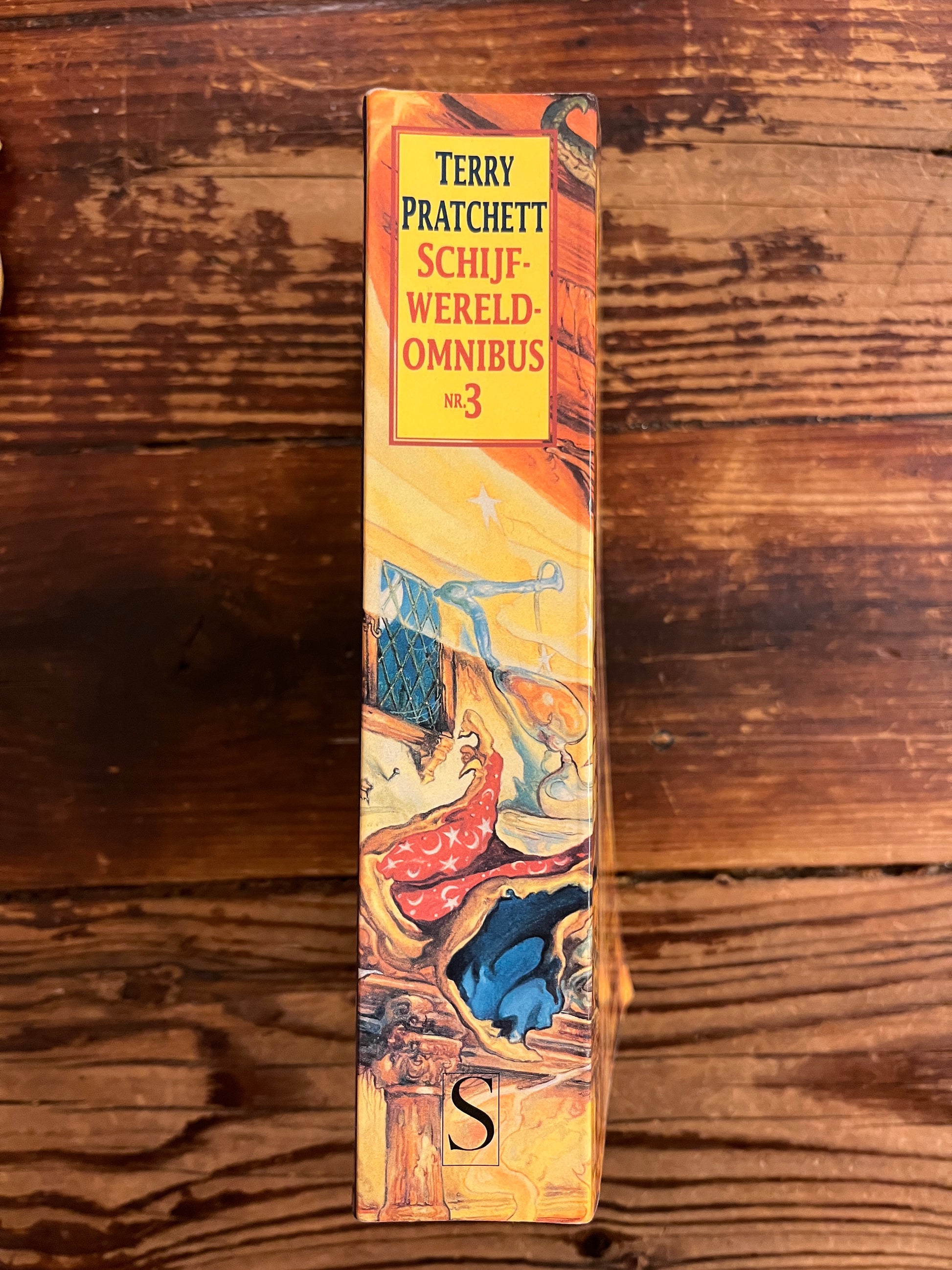 Rug van boek met de titel 'Terry Pratchett Schijfwereld Omnibus n 3' op een houten achtergrond