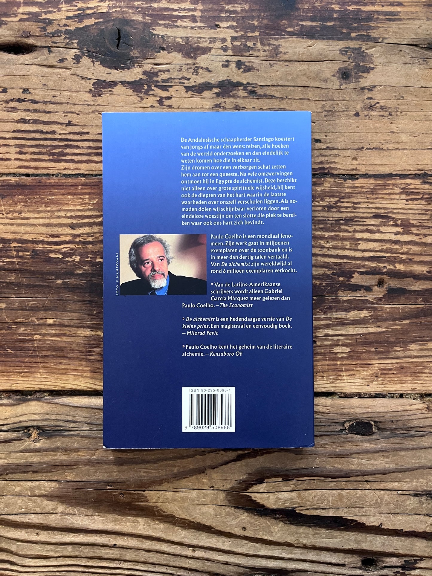 Achterkant van boek met de titel 'de Alchemist' door Paulo Coelho op een houten achtergrond