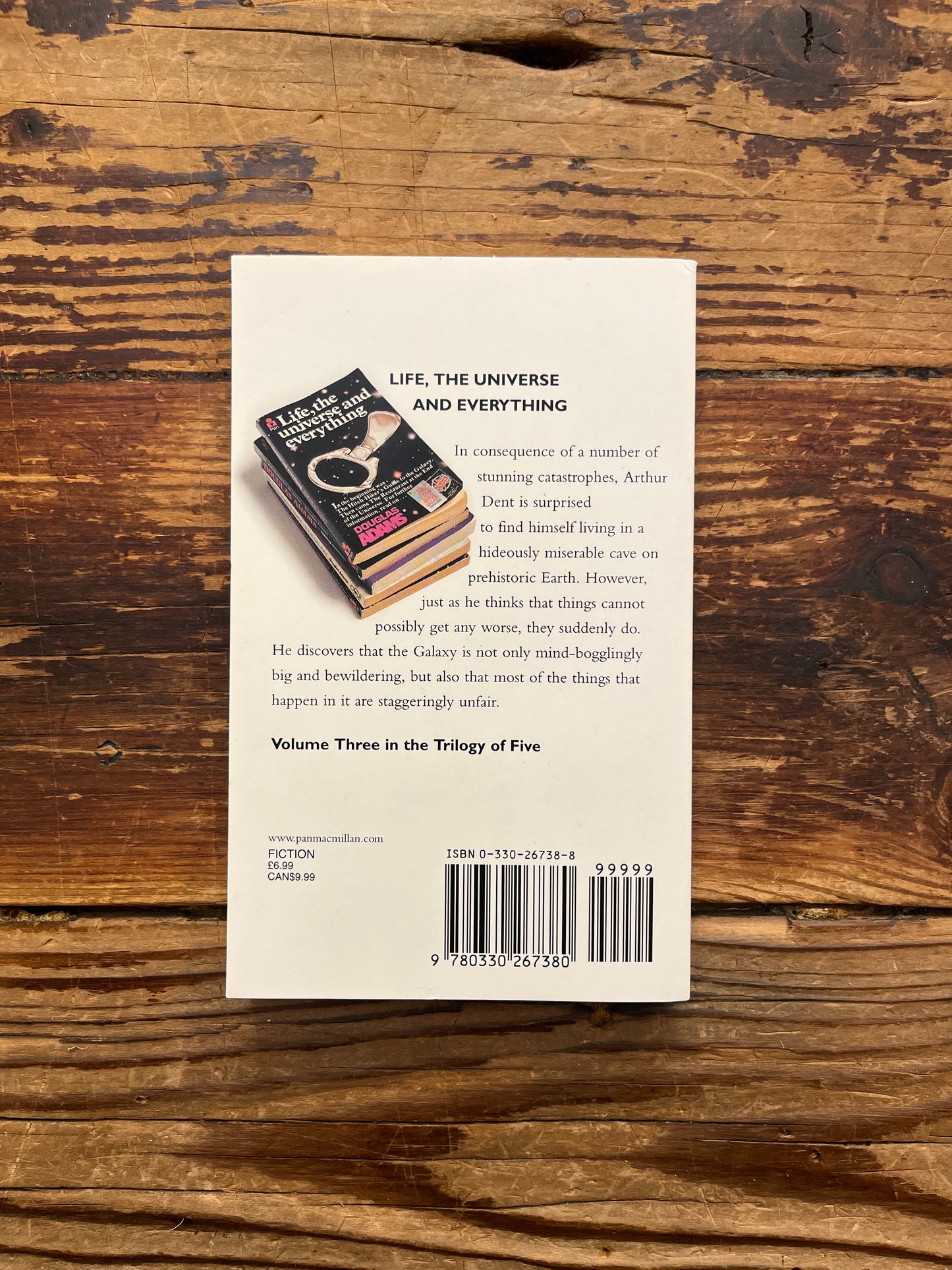 Book cover of 'Life, the Universe and Everything' by Douglas Adams on a wooden surface