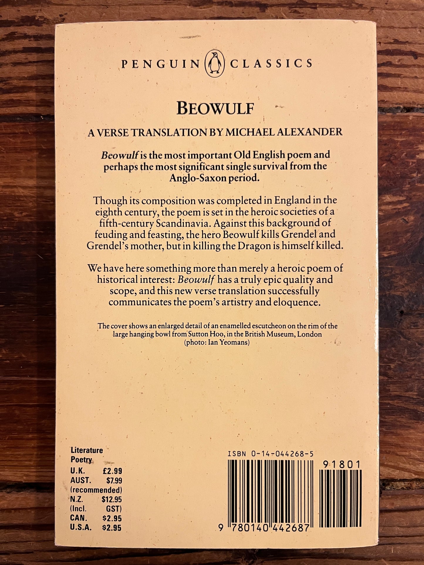 Back cover of a book titled 'Beowulf' by Michael Alexander on a wooden surface