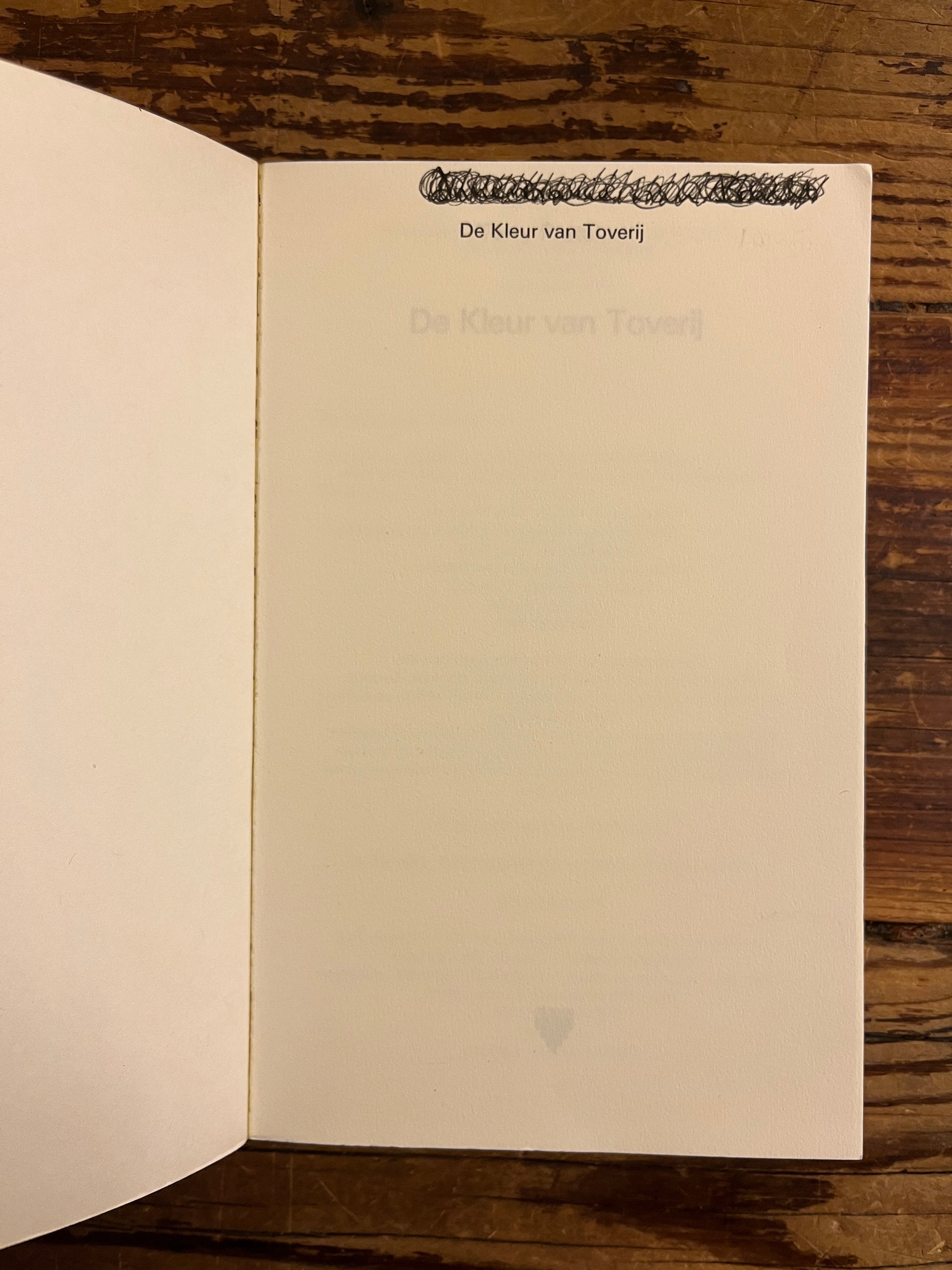 Open boek met de titel 'de kleur van Toverij' door Terry Prachett op houten achtergrond