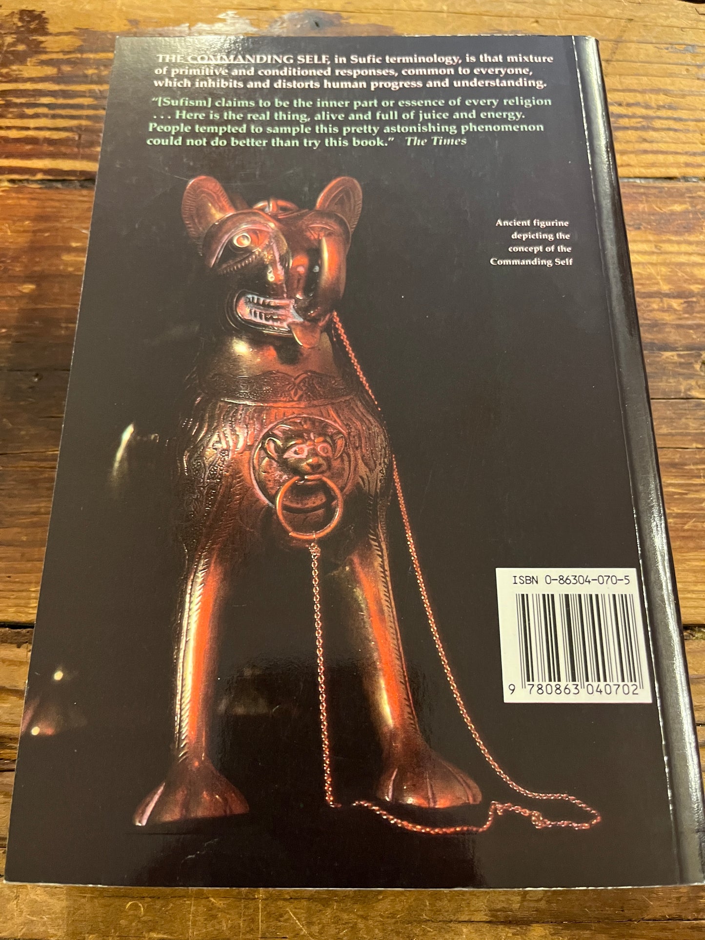 Back cover of a book titled 'The Commanding Self' by Idries Shah with a metallic figurine and text on a wooden surface