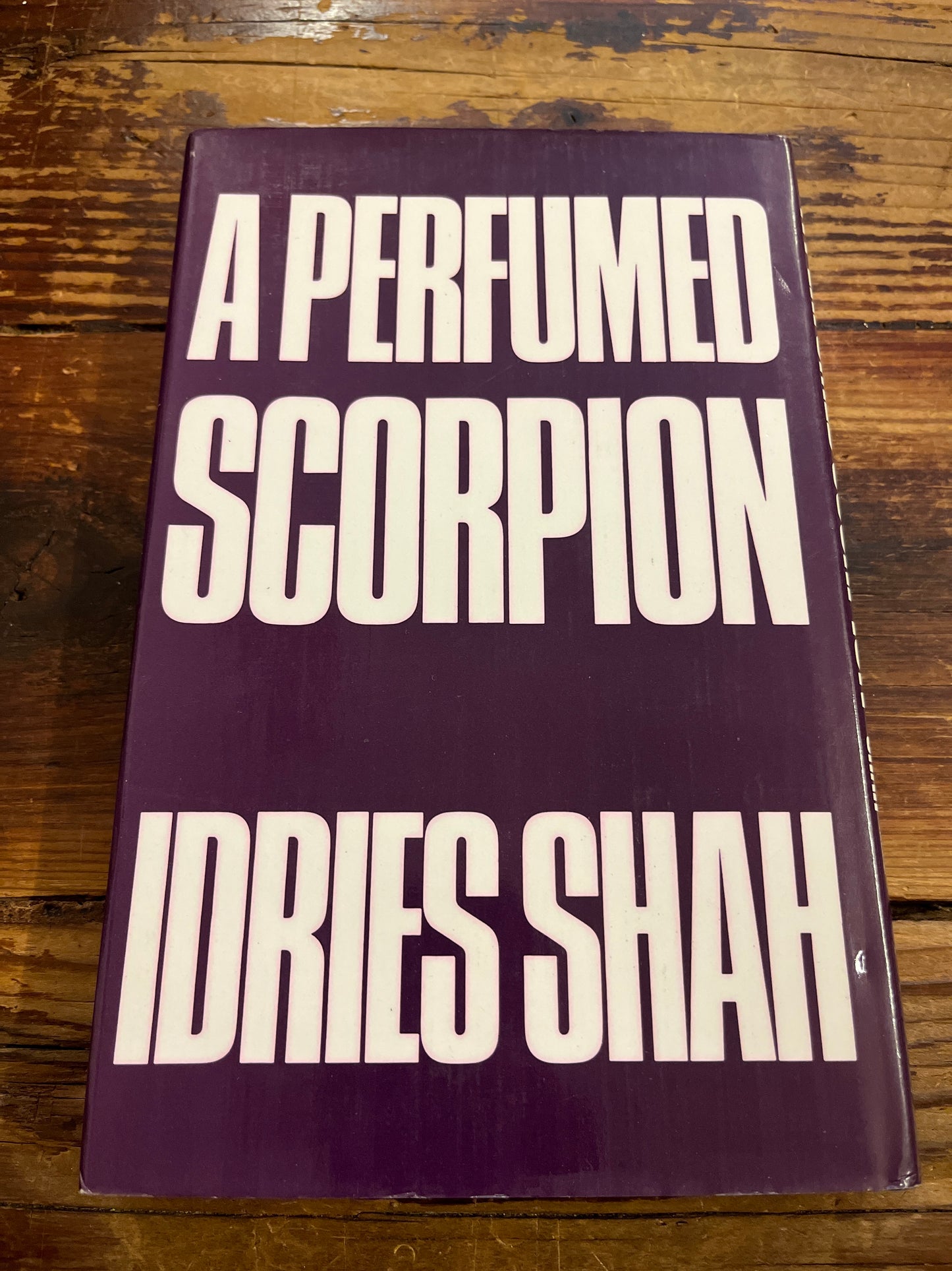 back cover of book titled 'A Perfumed Scorpion' by Idries Shah on a wooden surface