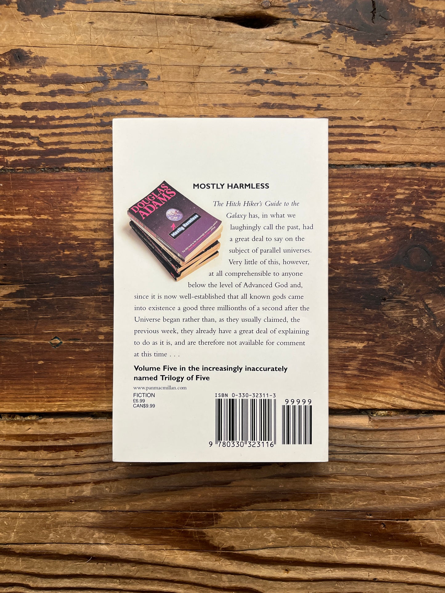 Back cover of book titled 'Mostly Harmless' by Douglas Adams on a wooden surface