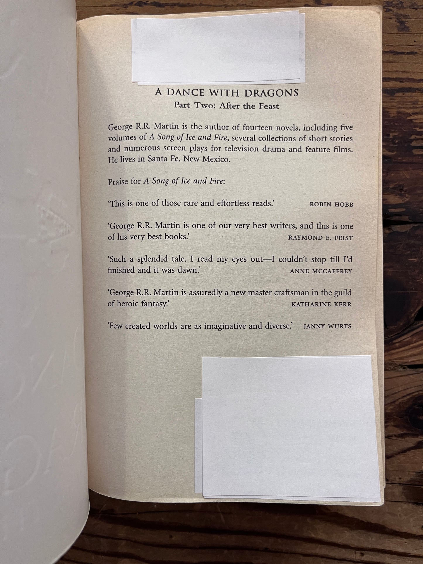 Corner with white sticker of the first page of Two books titled 'A Dance with Dragons' by George R.R. Martin on a wooden surface.