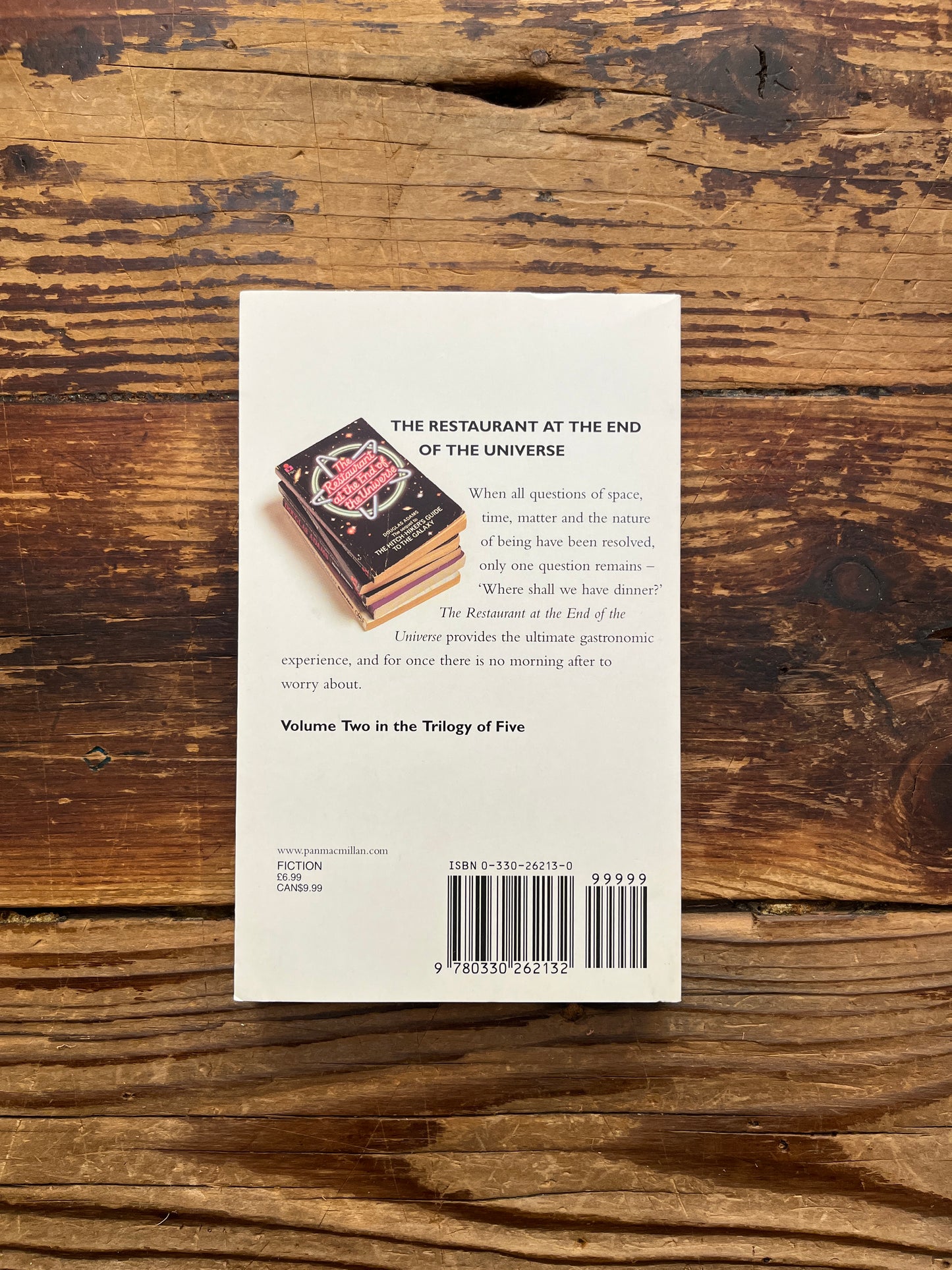 Book cover of 'The Restaurant at the End of the Universe' by Douglas Adams on a wooden surface