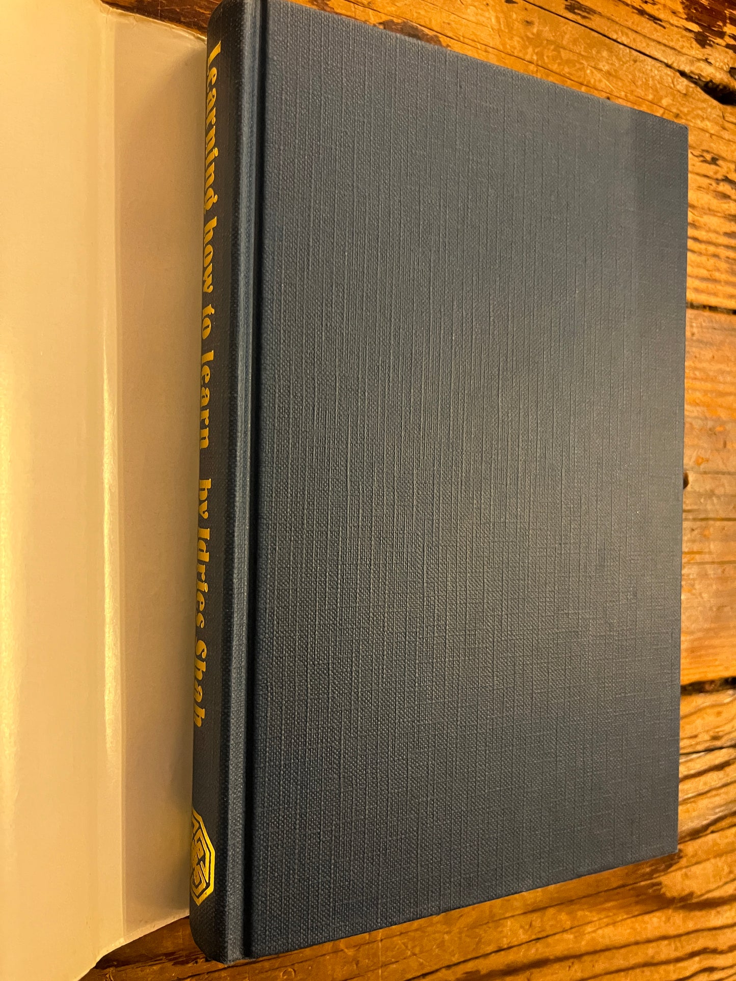 Book without dust-jacket with the title 'Learning how to learn' by Idries Shah in gilded letters on a wooden surface
