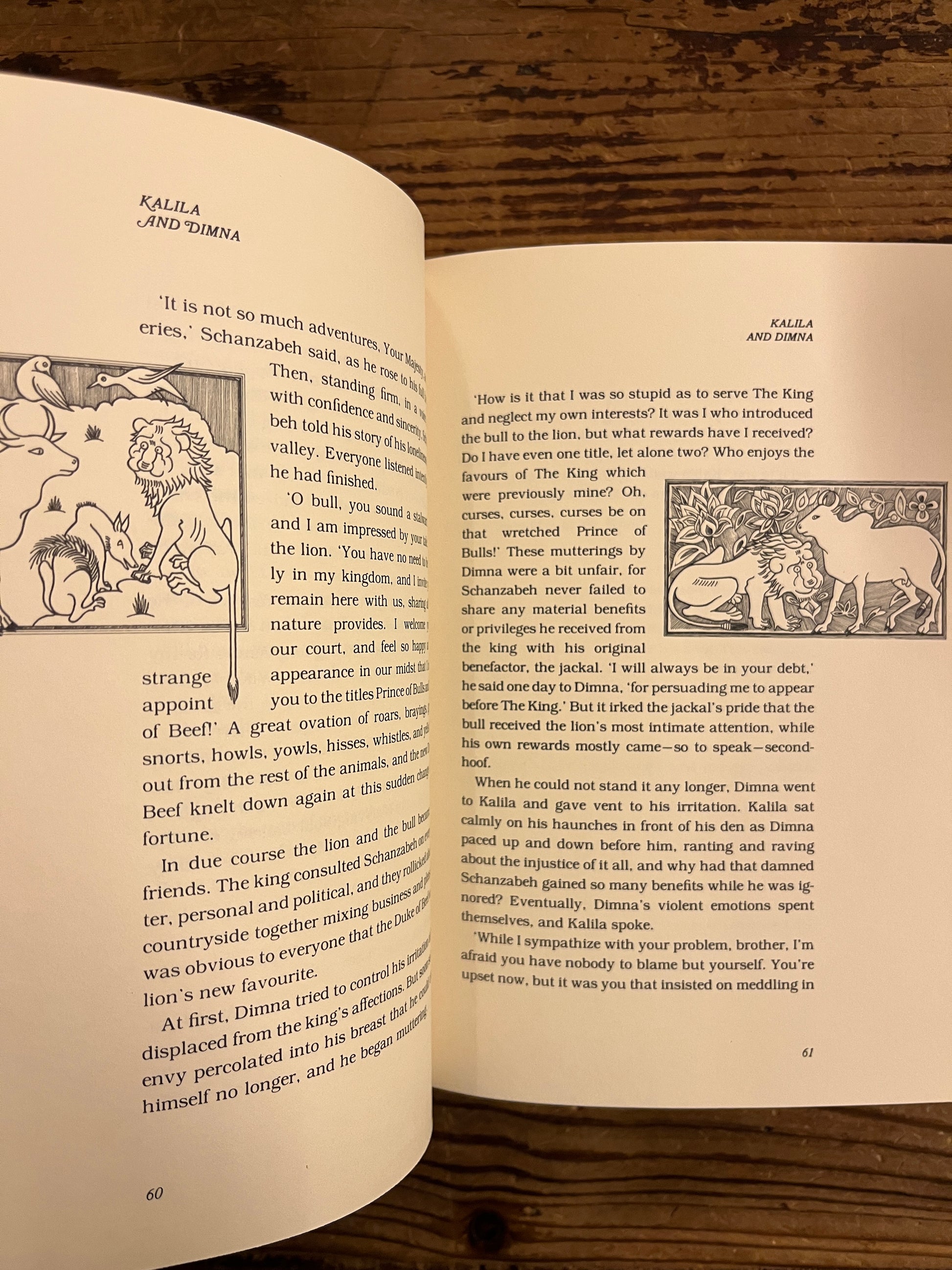 Open Book titled 'Kalila and Dimna, selected Fable of Bidpai' retold by Ramsay Wood on a wooden surface