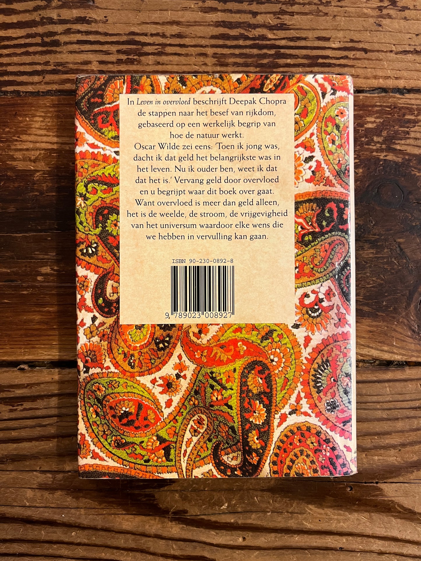 achterkant van Boek met de titel 'leven in overvloed' door Deepak Chopra op een houten achtergrond