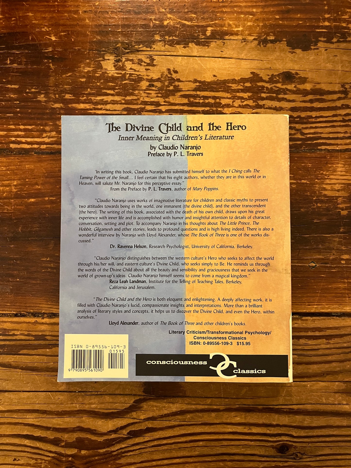 Back cover of book titled 'The Divine Child and the Hero' by Claudio Naranjo on a wooden surface