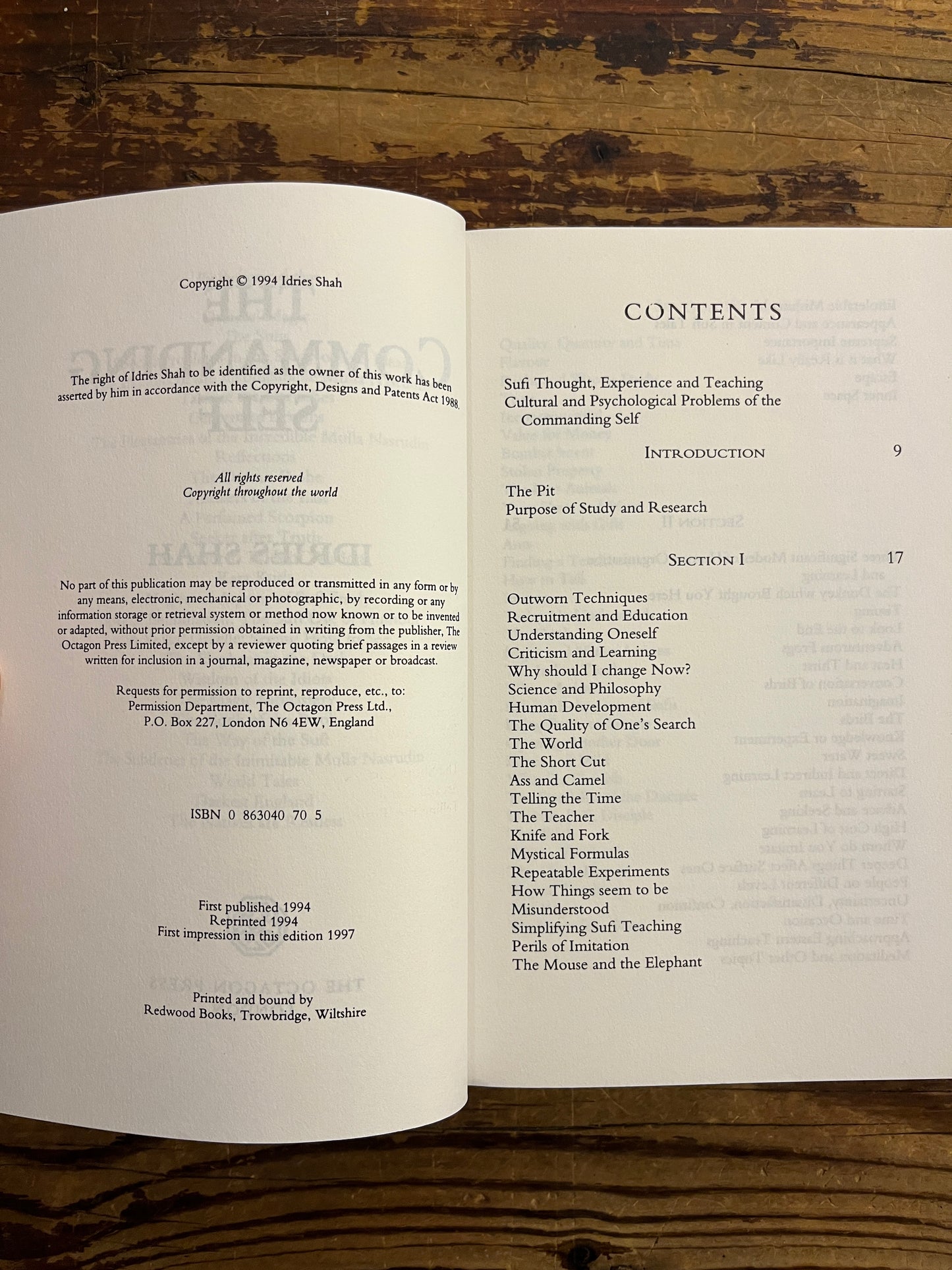 Open book titled 'The Commanding Self' by Idries Shah showing a table of contents on a wooden surface