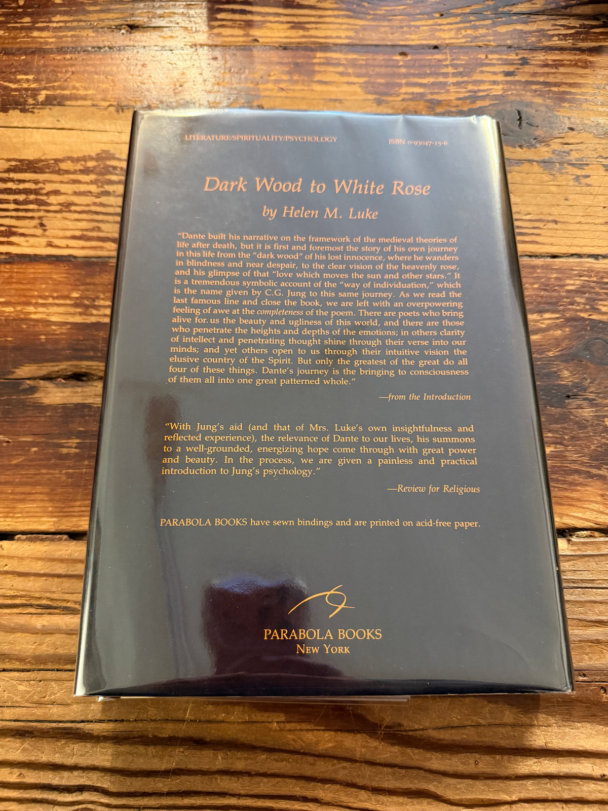 Back cover of a book with the title 'Dark Wood to White Rose, journey and transformation in Dante’s Divine Comedy' by Helen M. Luke on a wooden surface