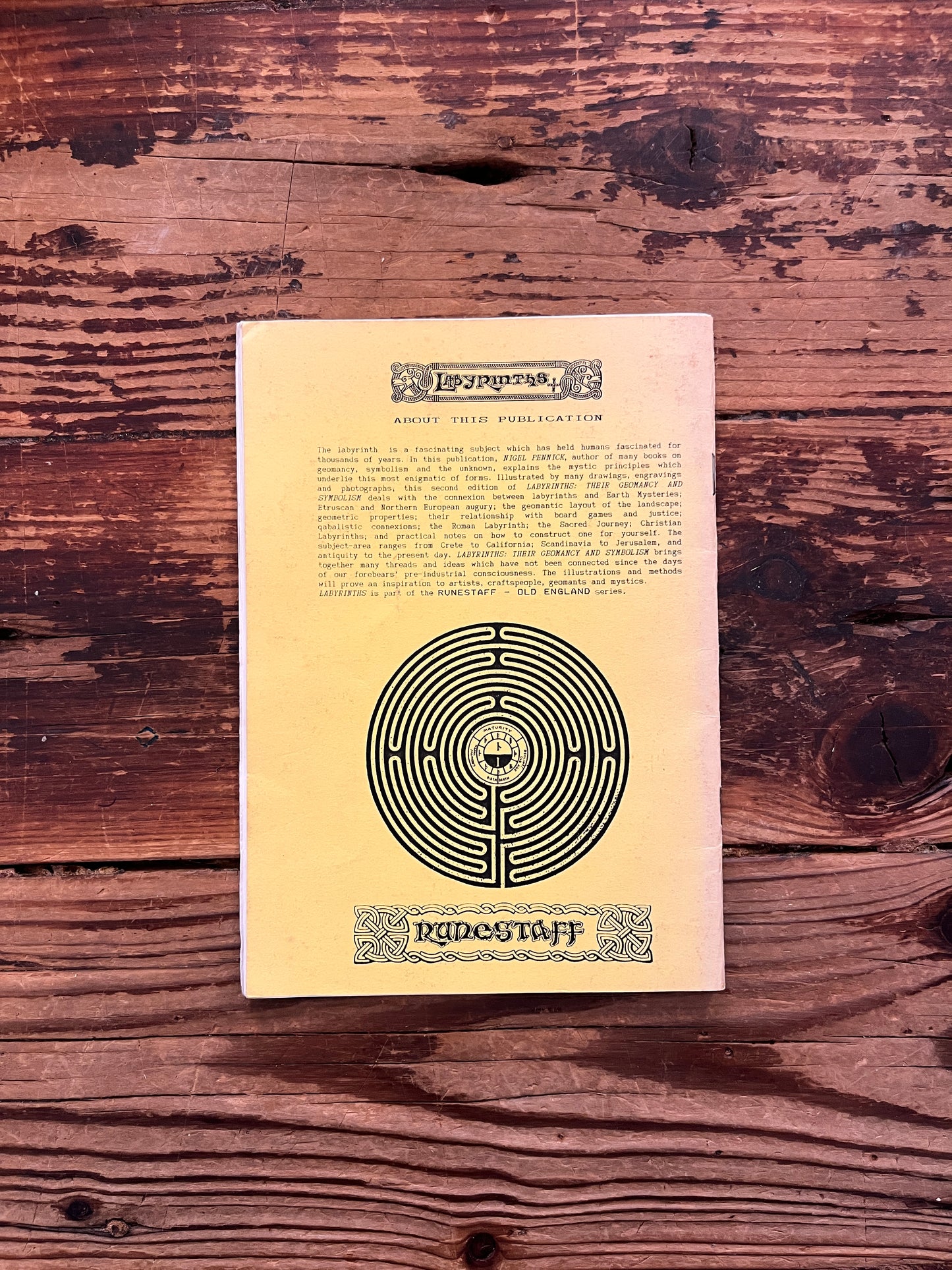 Back cover of booklet with the title 'Labyrinths, their geomancy and symbolism' by Nigel Pennick on a wooden surface