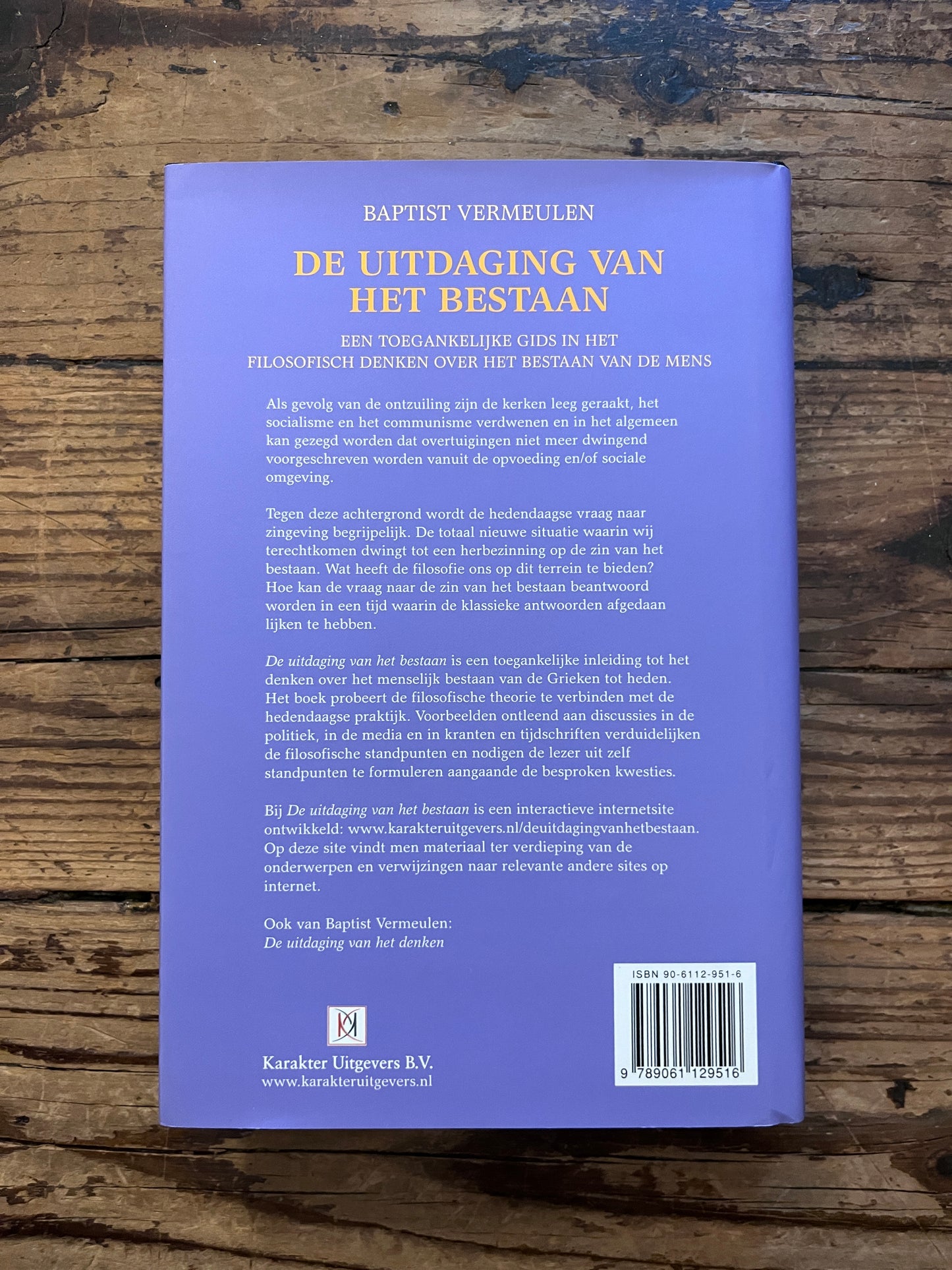foto van de backcover van het boek "De uitdaging van het bestaan"op houten achtergrond
