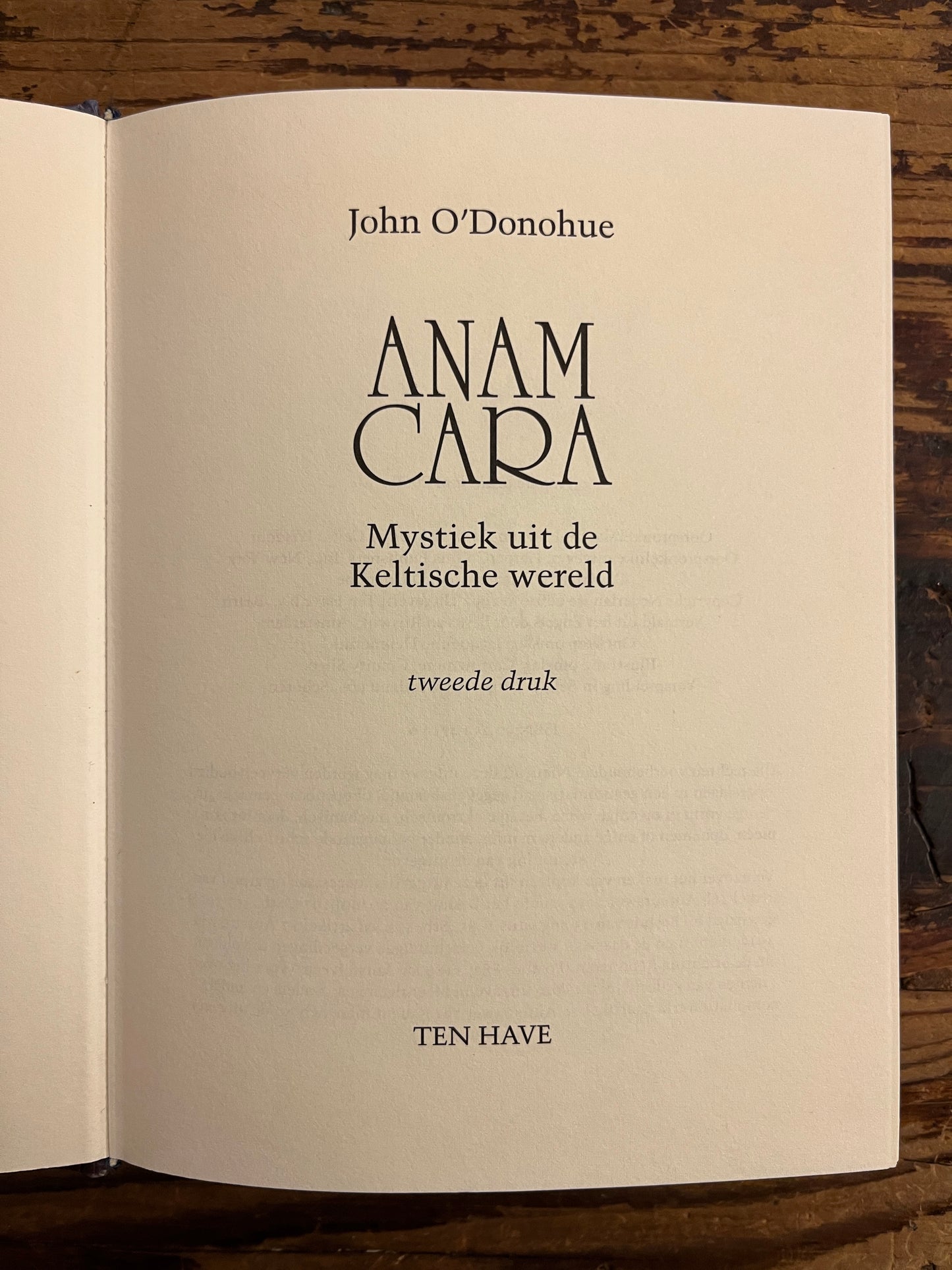 Open boek met de titel 'Anam Cara: Mystiek uit de Keltische wereld, tweede druk' door John O'Donohue op een houten achtergrond
