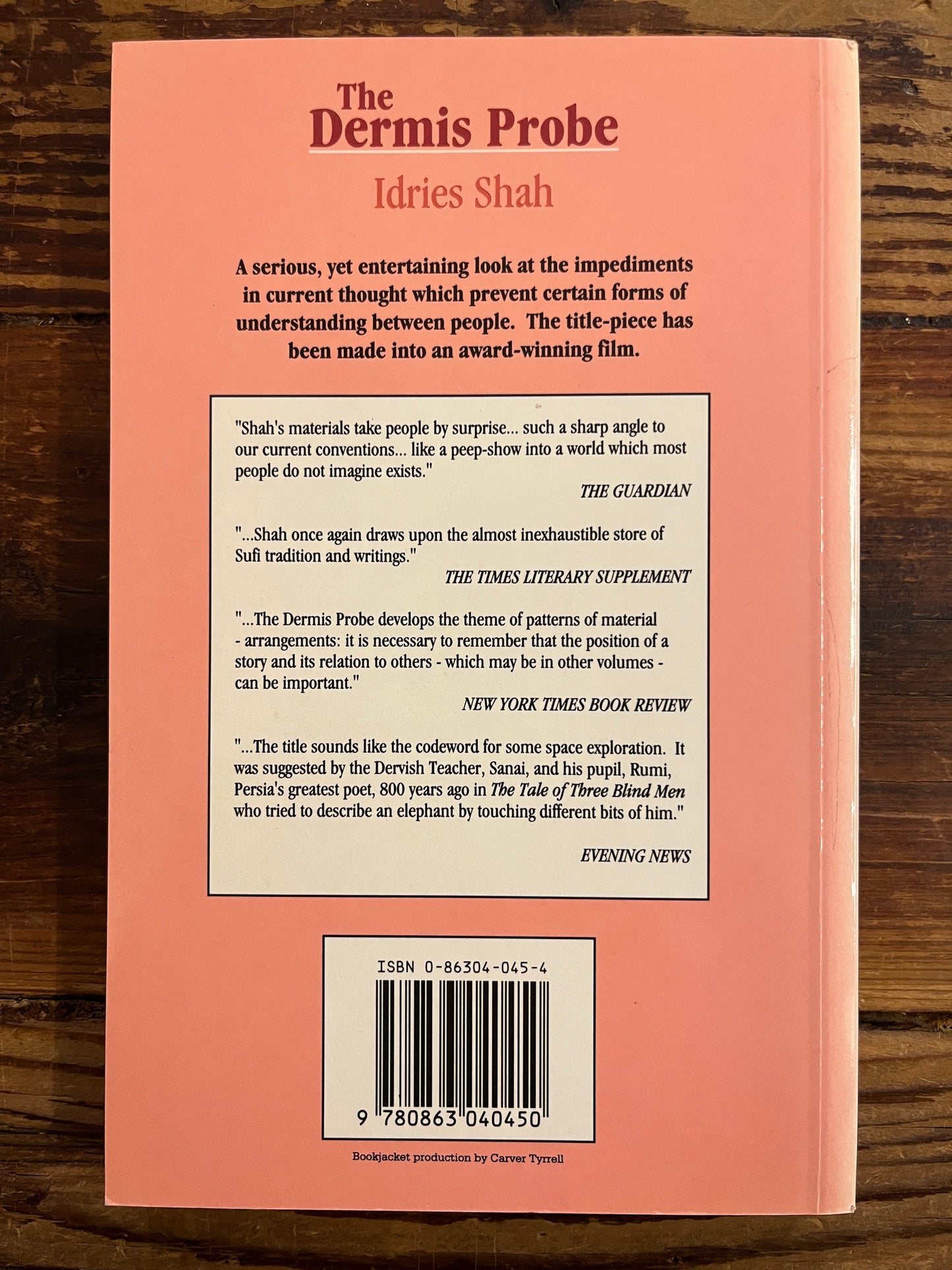 Back cover of a book 'The Dernis Probe' by Idries Shah with text and a barcode on a wooden surface
