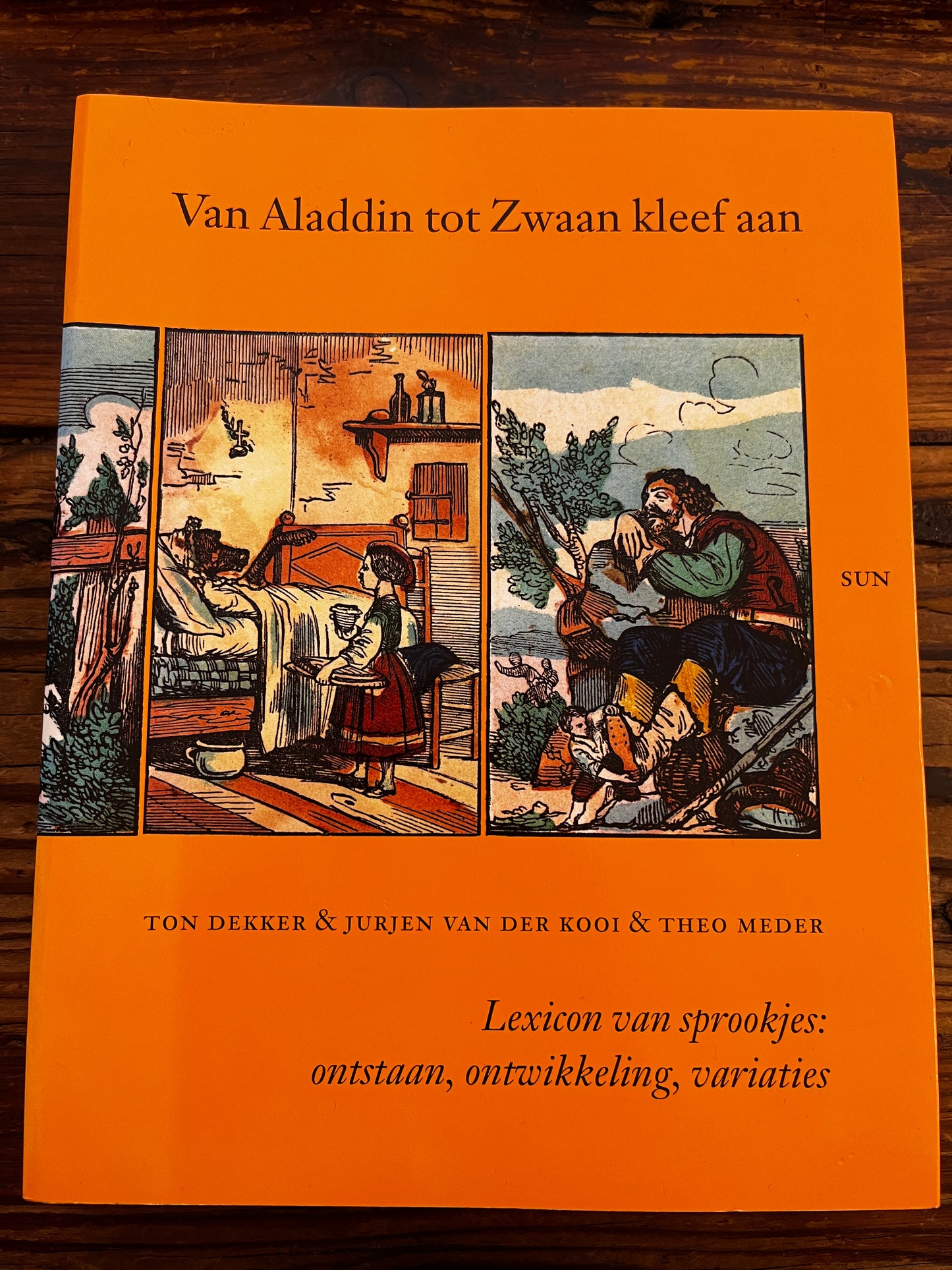 Voorkant van boek met titel 'Van Aladdin tot Zwaan kleef aan' op houten achtergrond