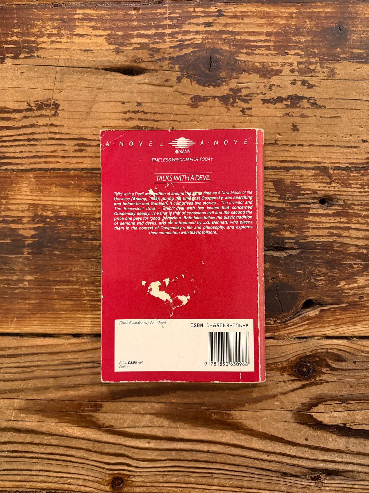Back cover of a book with the title 'Talks with a Devil' by P.D. Ouspensky, lying on a wooden surface
