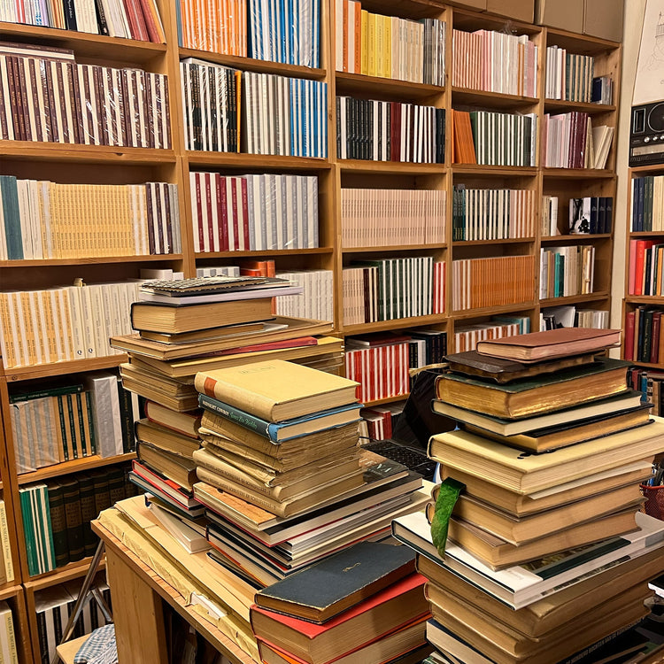 stack of books in front of a back ground of bookshelves in a bookstore