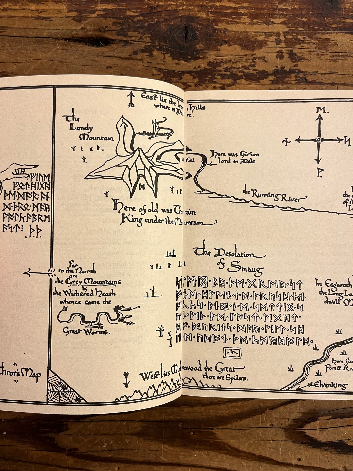 Open book showing the map of book titled 'The Hobbit' by J.R.R. Tolkien on a wooden surface