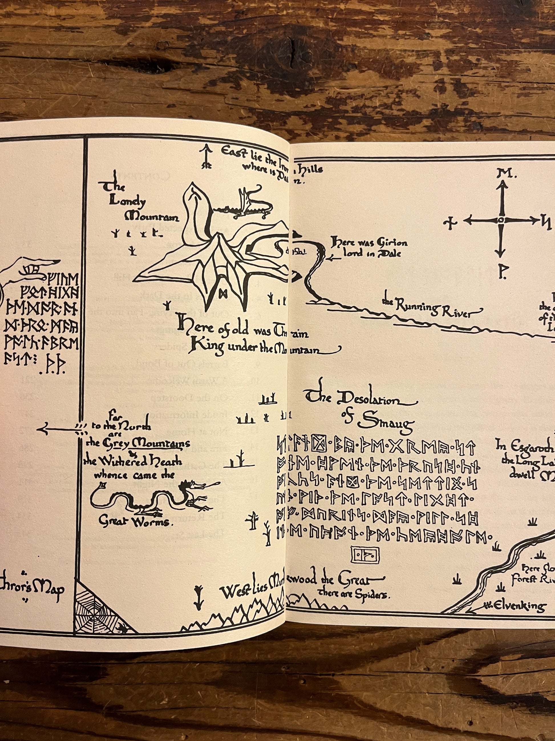 Open book showing the map of book titled 'The Hobbit' by J.R.R. Tolkien on a wooden surface