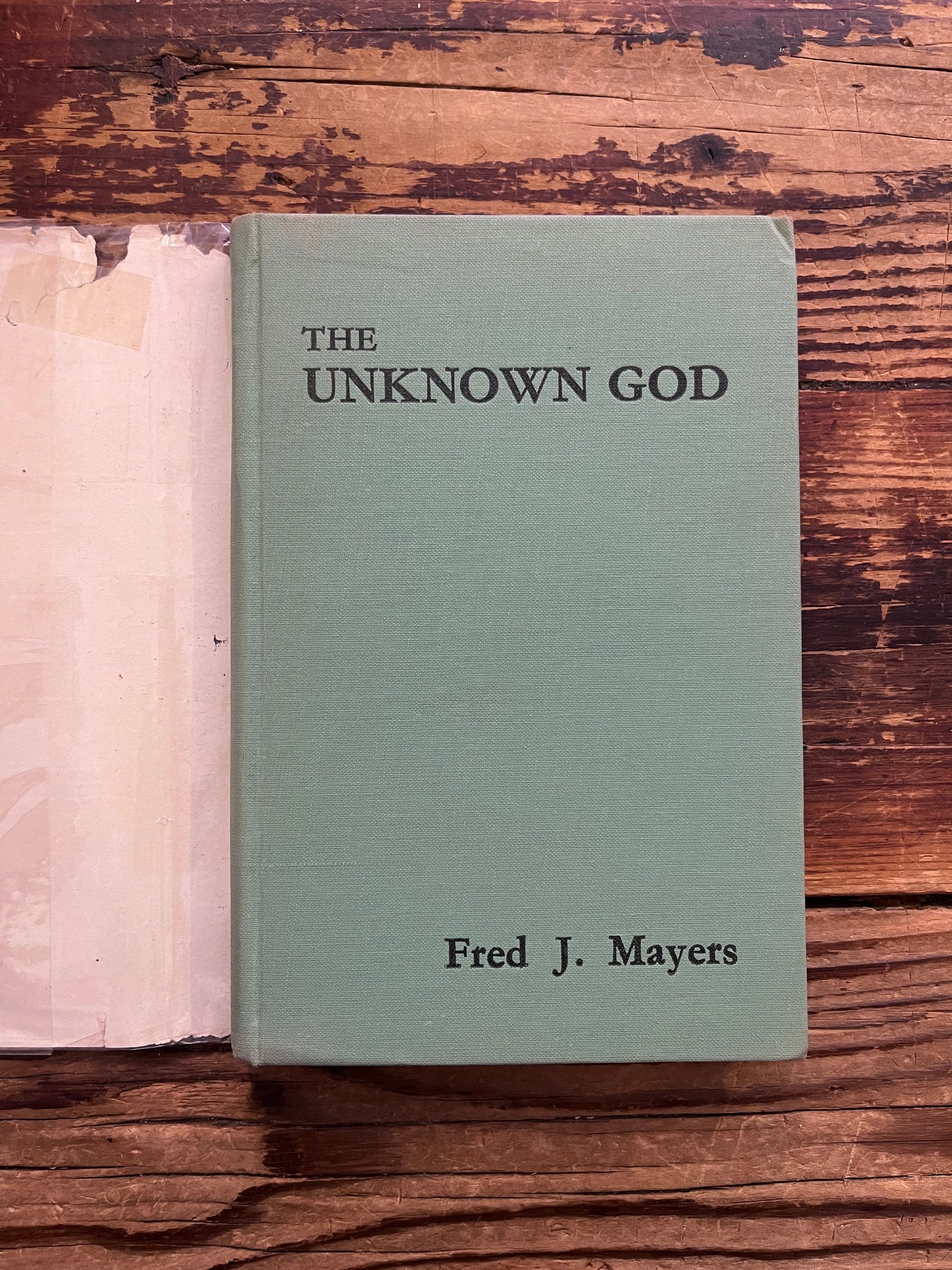 Frontcover without dust jacket of book titled 'Ain Soph The Unknown God' by F. J. Mayers on a wooden surface