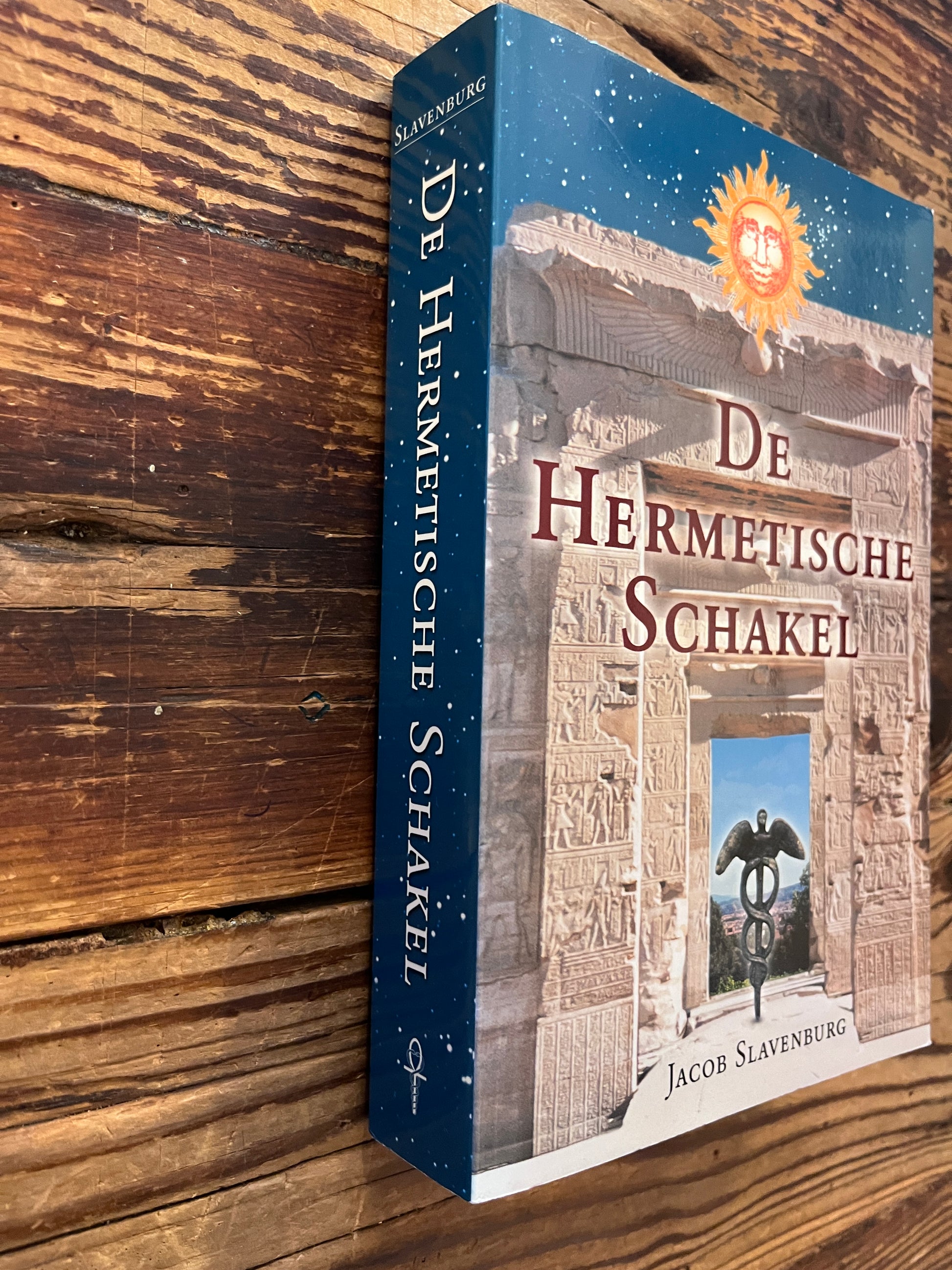 Voorkant en rug van boek met de titel 'de Hermetische Schakel' door Jacob Slavenburg op een houten achtergrond 