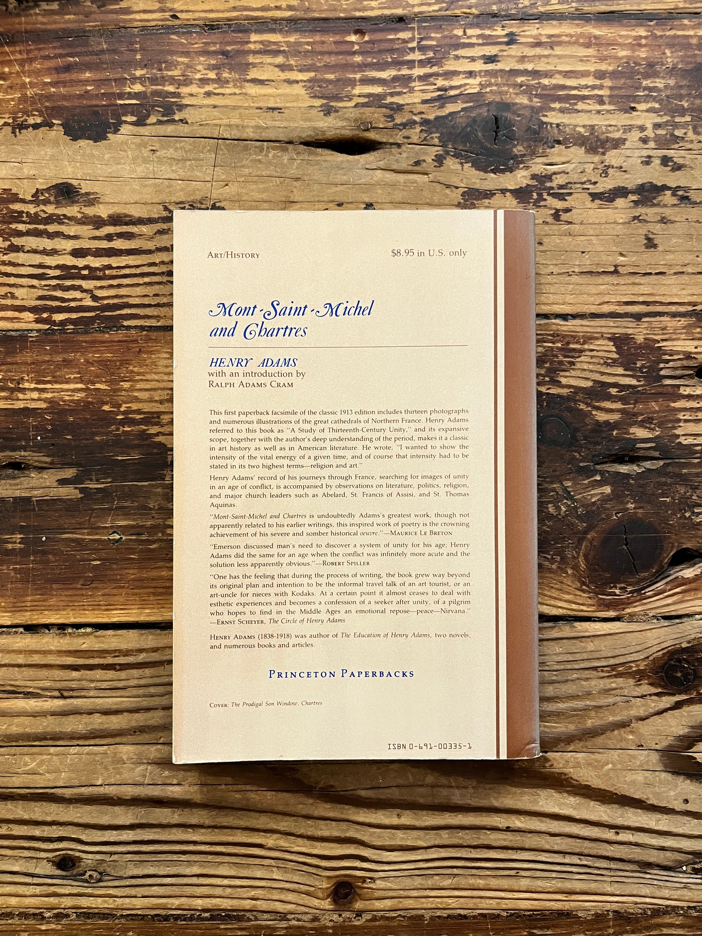 Back cover of a book titled 'Mont Saint-Michel and Chartres' by Henry Adams on a wooden surface