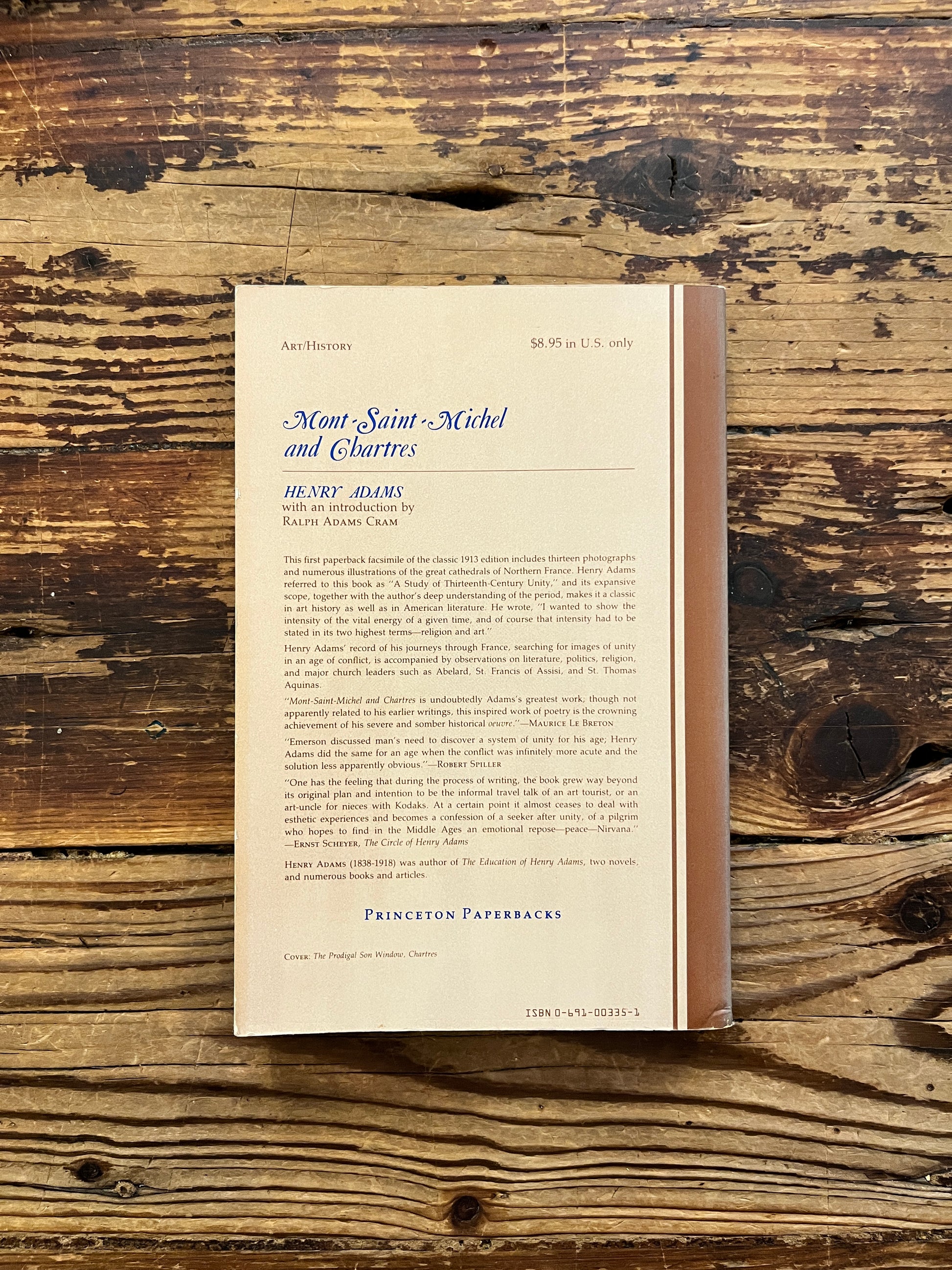 Back cover of a book titled 'Mont Saint-Michel and Chartres' by Henry Adams on a wooden surface