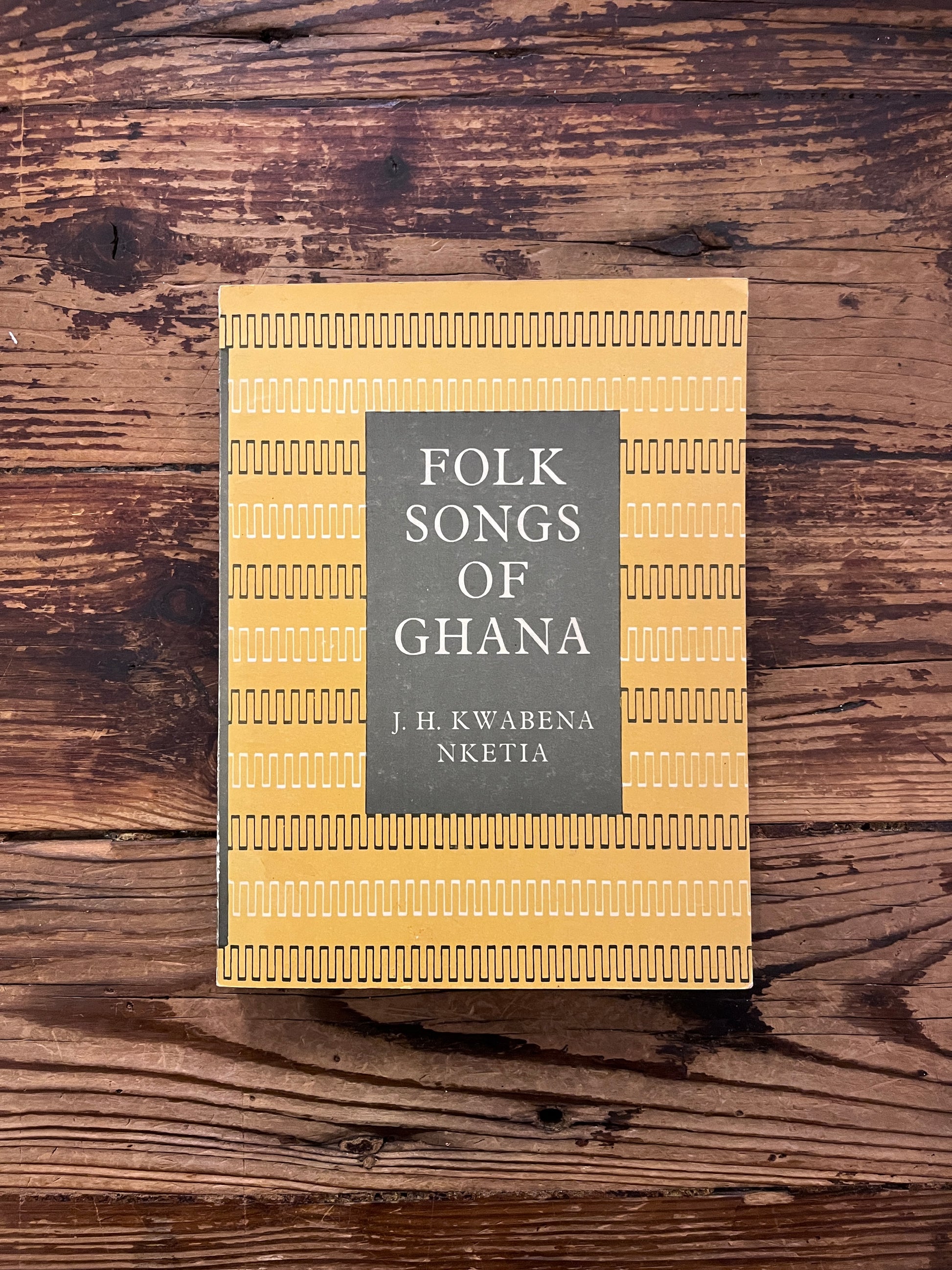 Front cover of book titled 'Folk Songs of Ghana' by J.H. Kwabena Nketia on a wooden surface 
