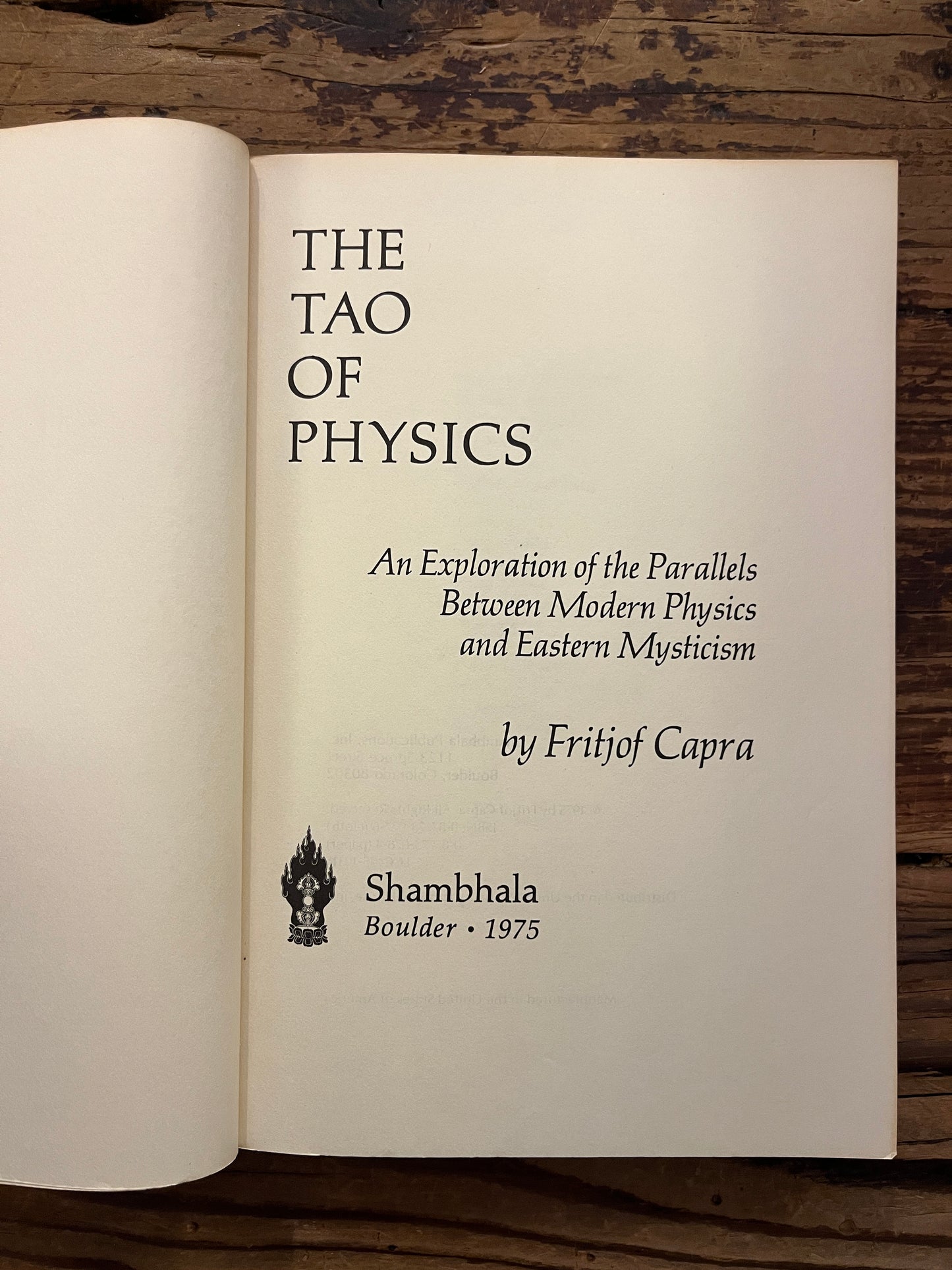 Open book titled 'The Tao of Physics' by Fritjof Capra on a wooden surface