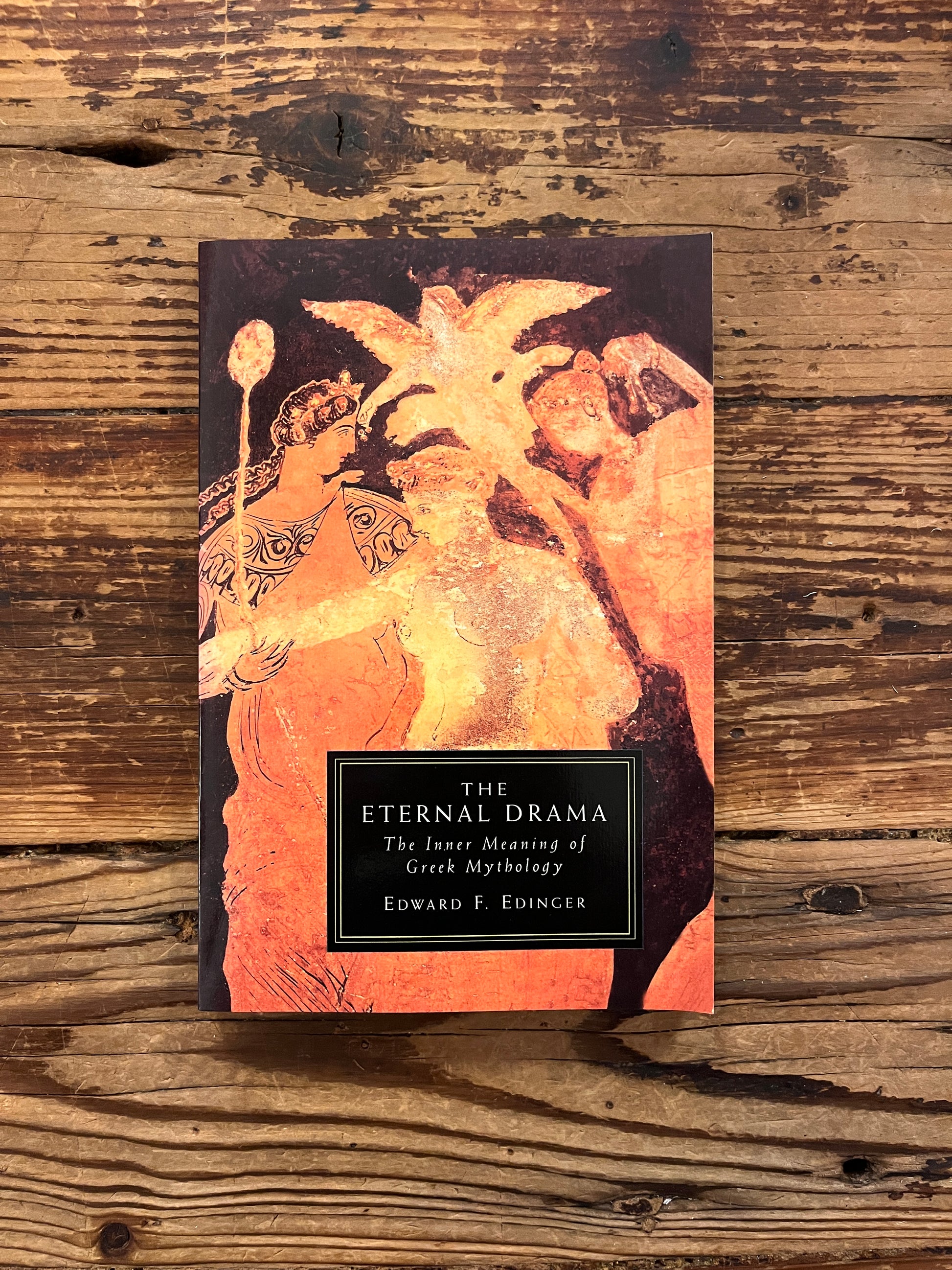 Front cover of book titled 'The Eternal Drama: Greek Mythology' by Edward T. Edinger lying on a wooden surface