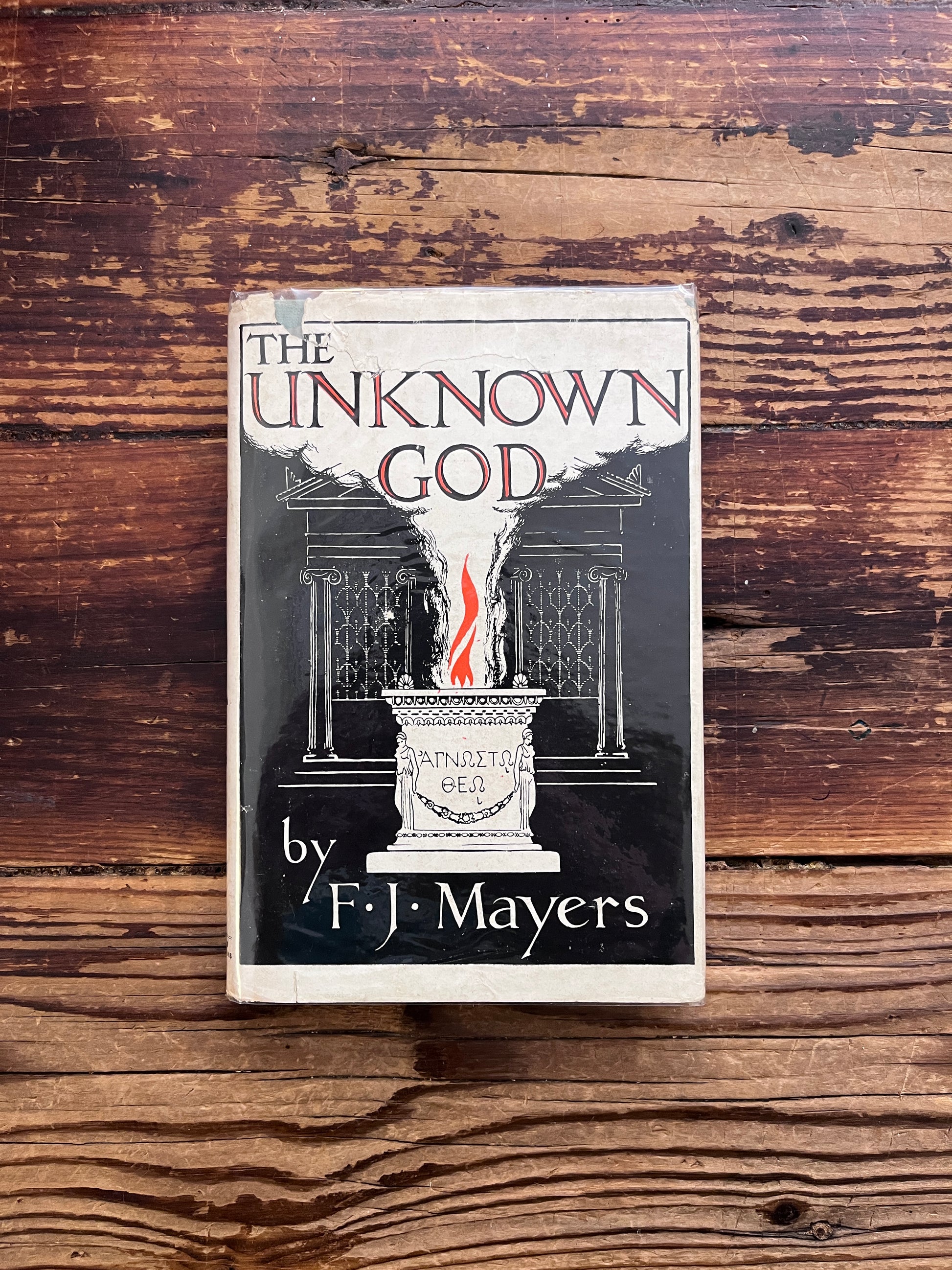 Front cover of a book titled 'Ain Soph The Unknown God' by F. J. Mayers on a wooden surface