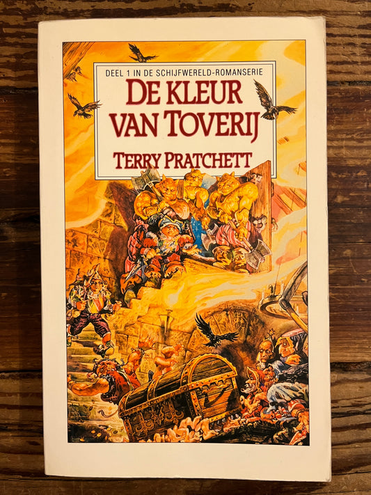 Voorkant van boek met de titel 'de kleur van Toverij' door Terry Prachett op houten achtergrond 