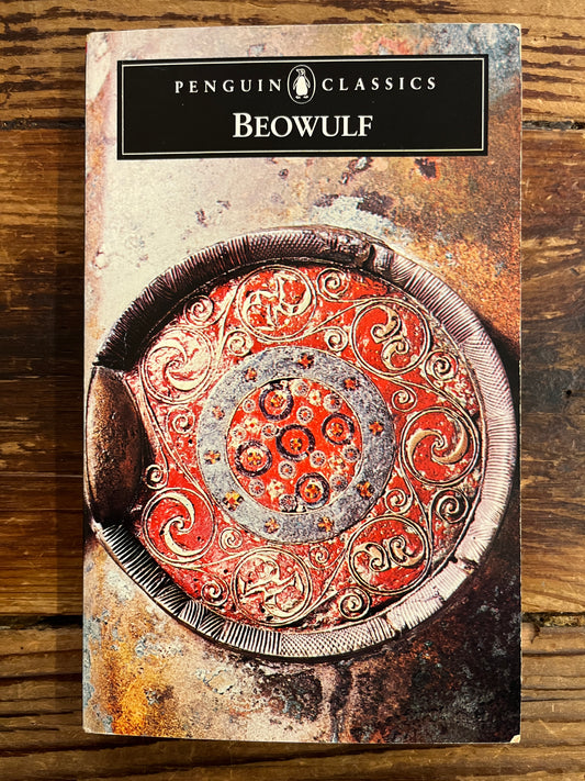 Book cover of 'Beowulf' by Penguin Classics on a wooden surface, the cover shows an enlarged detail of an enamelled escutcheon on the rim of the large hanging bowl from Sutton Hoo, in the British Museum, London, photo: lan Yeomans 